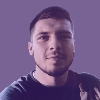 Close-up portrait of a young man with short dark hair and trimmed beard, looking directly at the camera against a solid purple background.