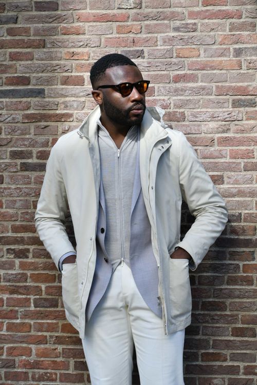 Stylish man in light-colored outfit and sunglasses posing against a brick wall