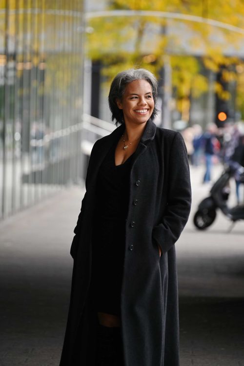 Confident woman smiling in a black coat with an urban city background and fall trees