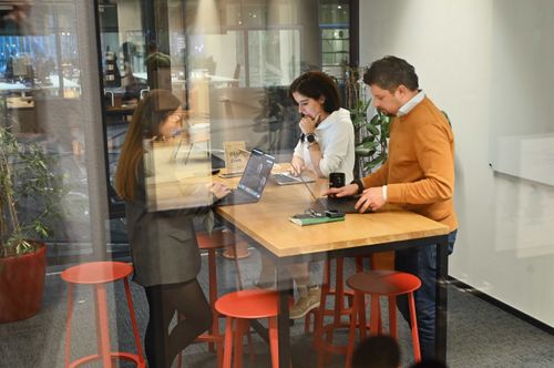 Team of professionals collaborating in a glass-walled coworking space using laptops and digital tools