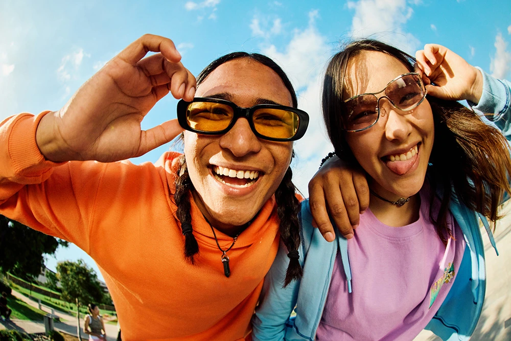 Image of a girl smiling close to the camera wearing glasses with hands on her face