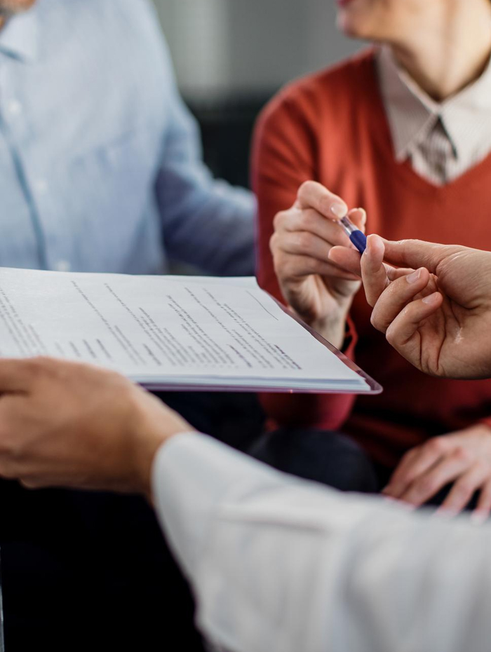 Person übergibt anderen Person einen Stift, während ein Dokument mit Text auf einem Klemmbrett gehalten wird.