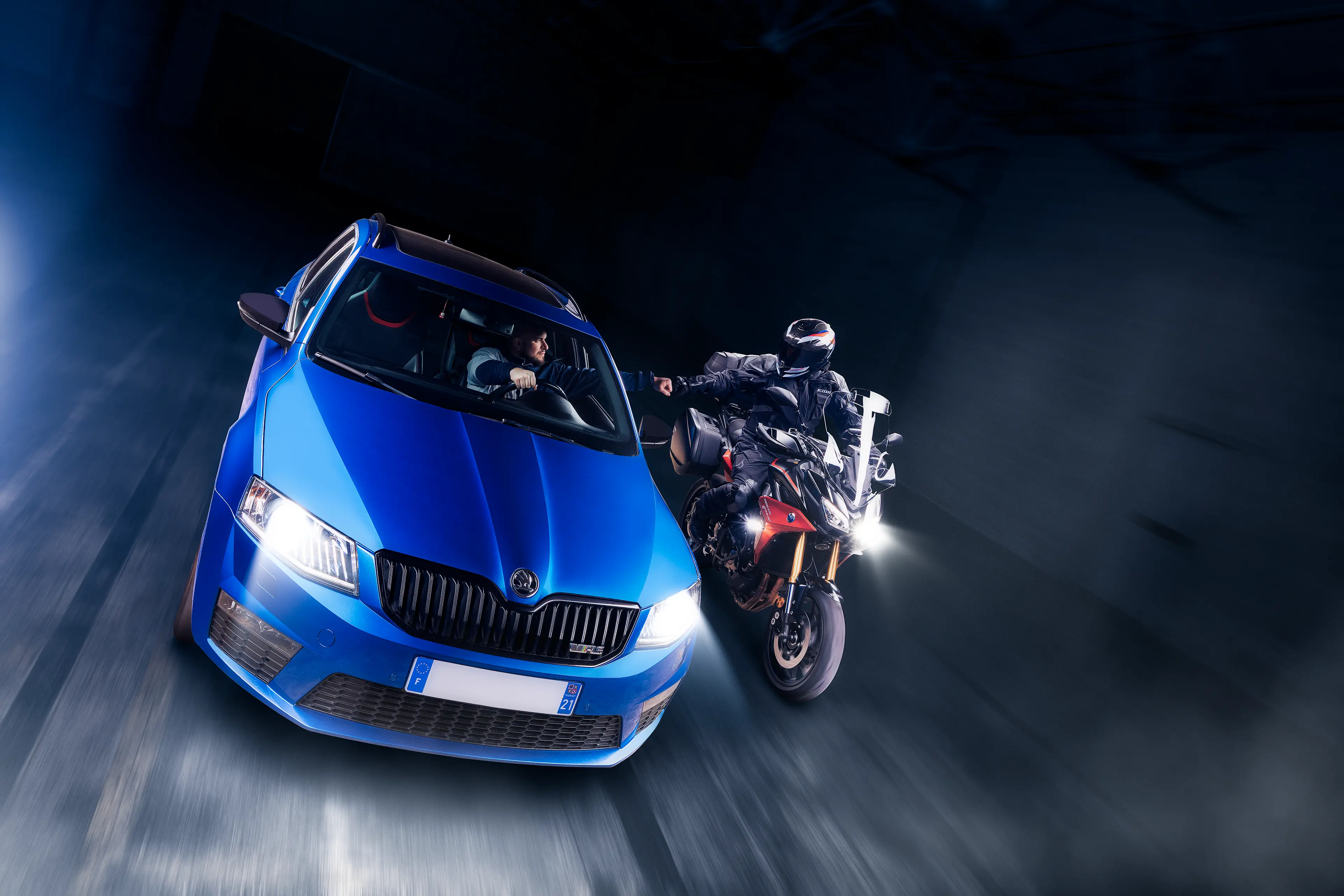 Skoda Octavia VRS break bleue de 3/4 avant avec une Yamaha Tracer 900GT rouge, roulant ensemble dans un entrepĂŽt sombre en light painting