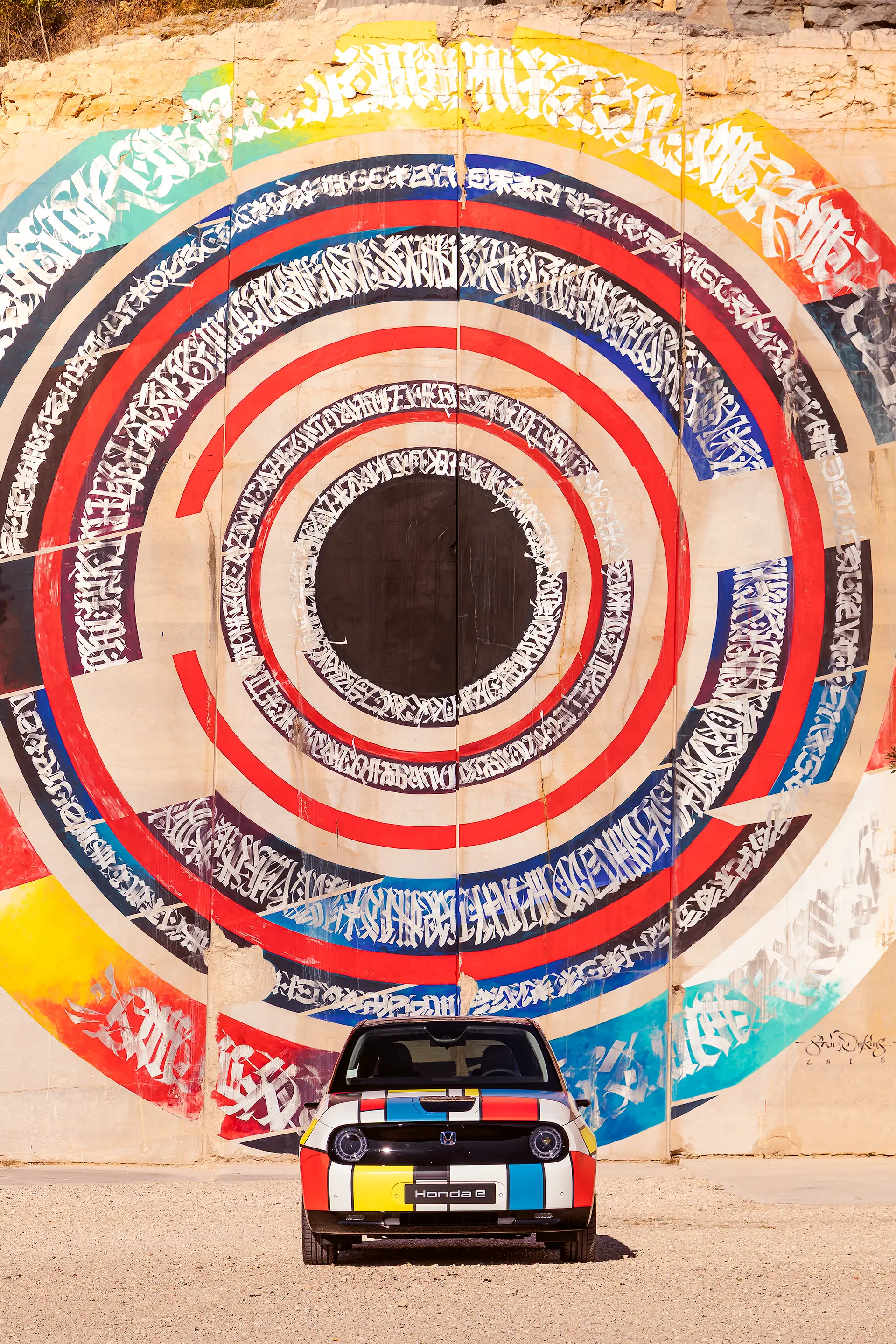 Honda E avec covering Mondrian de face devant une œuvre de street art