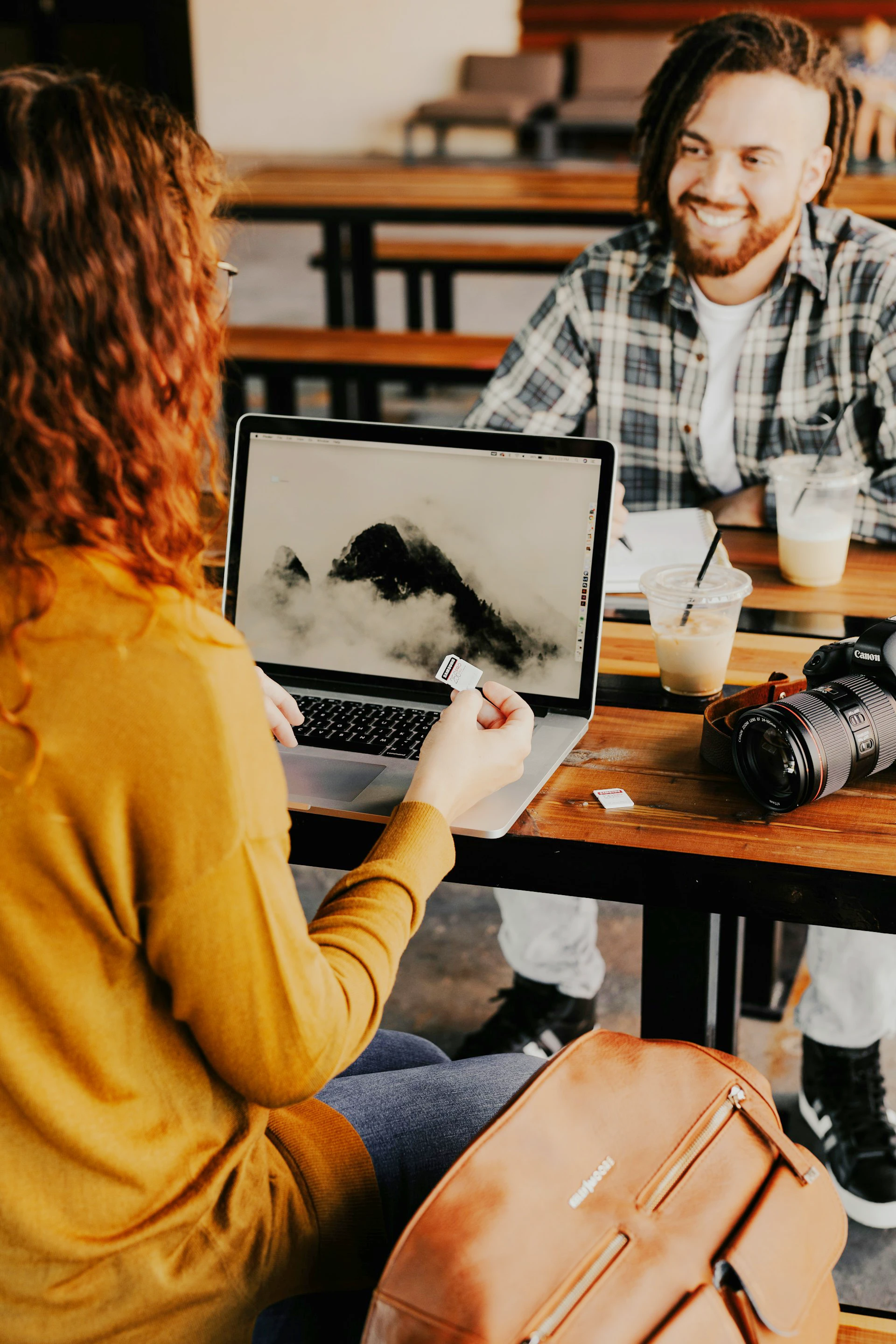Un homme et une femme assis à une table discutant de photographie avec un reflex et un ordinateur portable sur la table