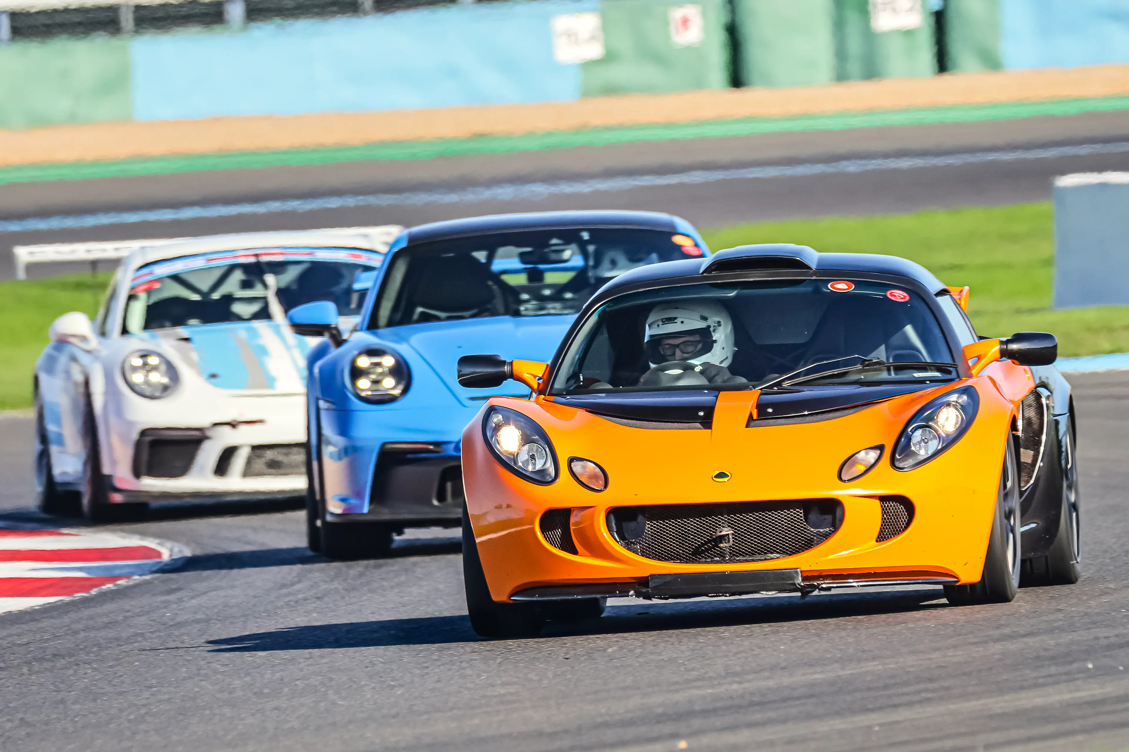 Lotus Elise S3 Orange, Porsche 911 992 GT3 bleue et Porsche 911 991 GT3 Cup blanche sur le circuit de Nevers Magny-Cours