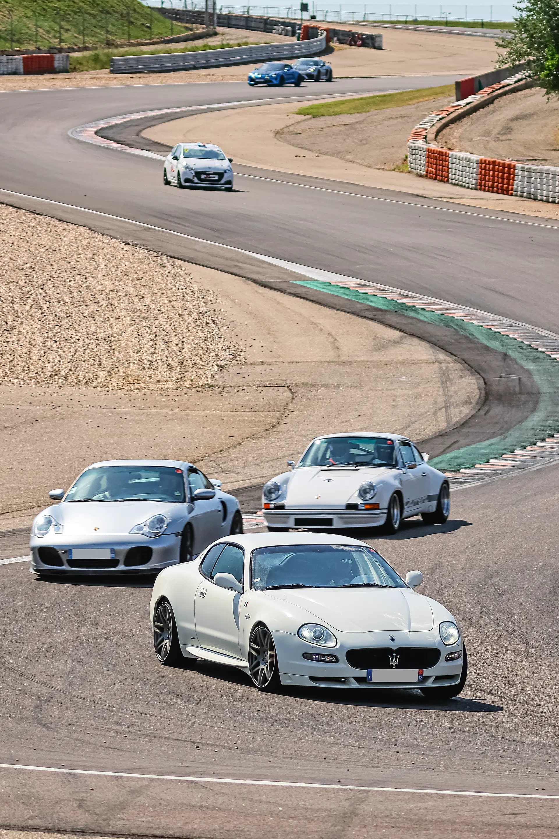 Maserati Gran Turismo blanche, Porsche 911 996 grise, Porsche 911 930 blanche et d'autres voitures sur le circuit de Lédenon