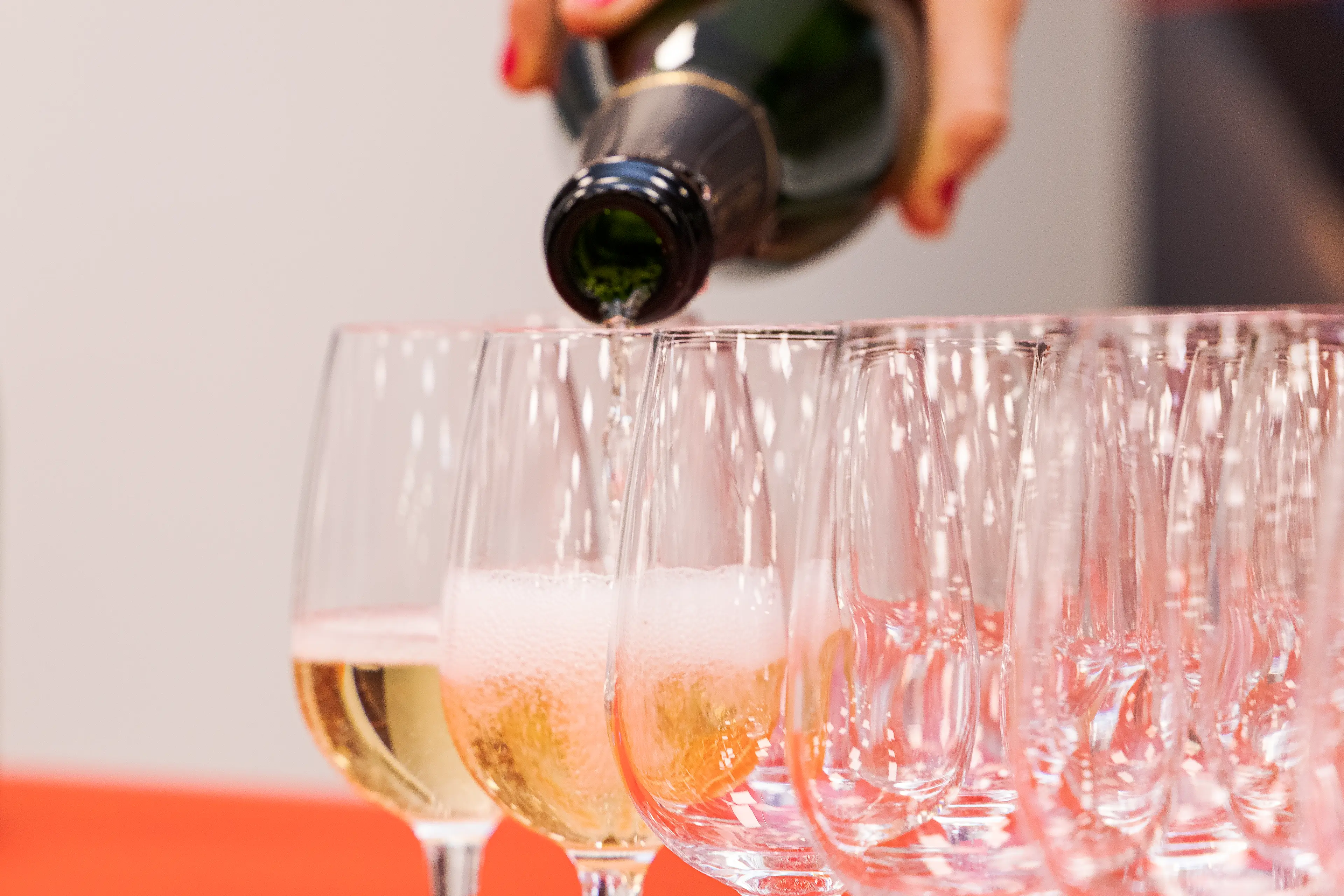 Plusieurs coupes de champagne alignées et une bouteille remplissant un des verres