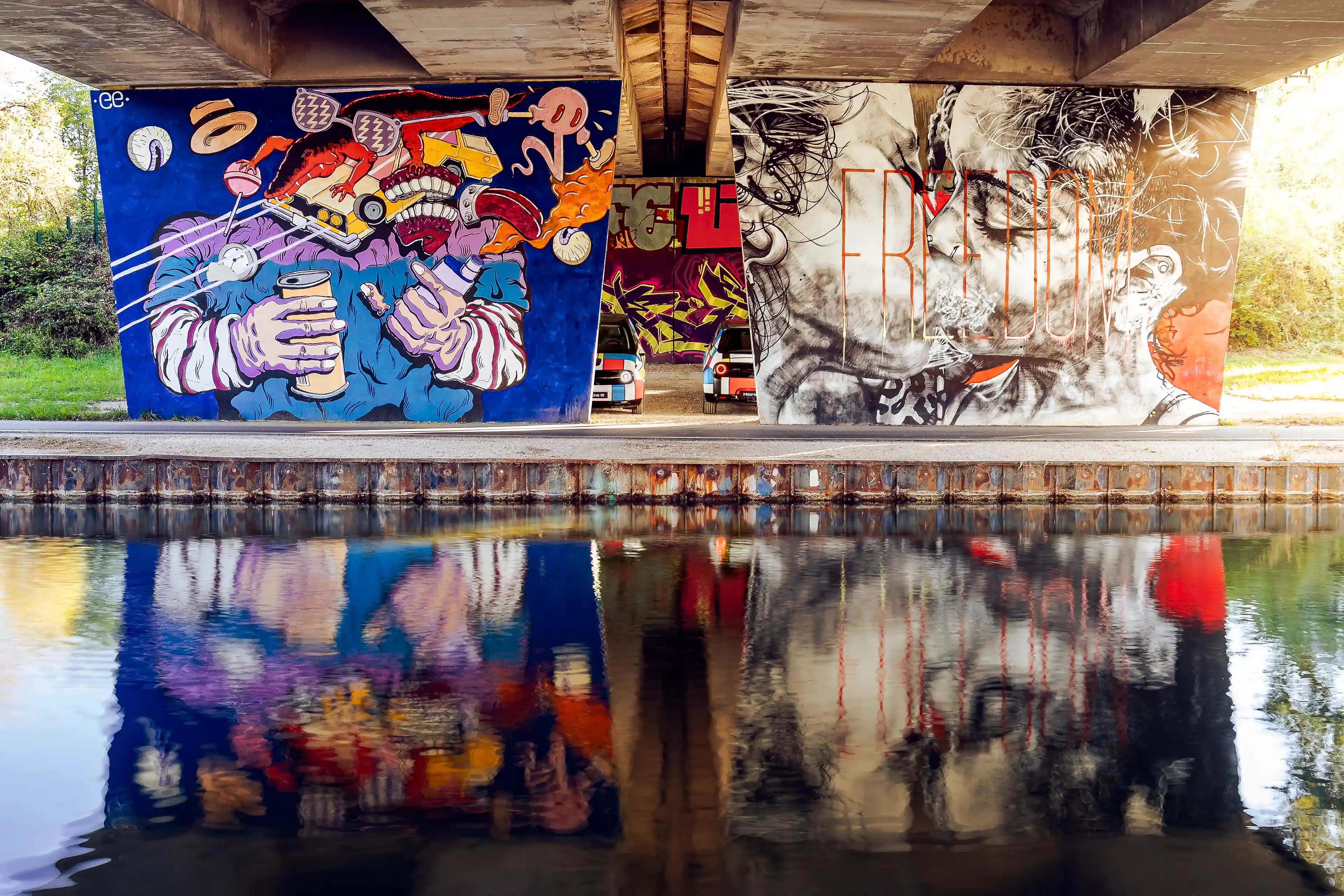 Deux Honda E avec leur déco Mondrian cachée derrière des plaques de béton avec des œuvres de street art sous un pont