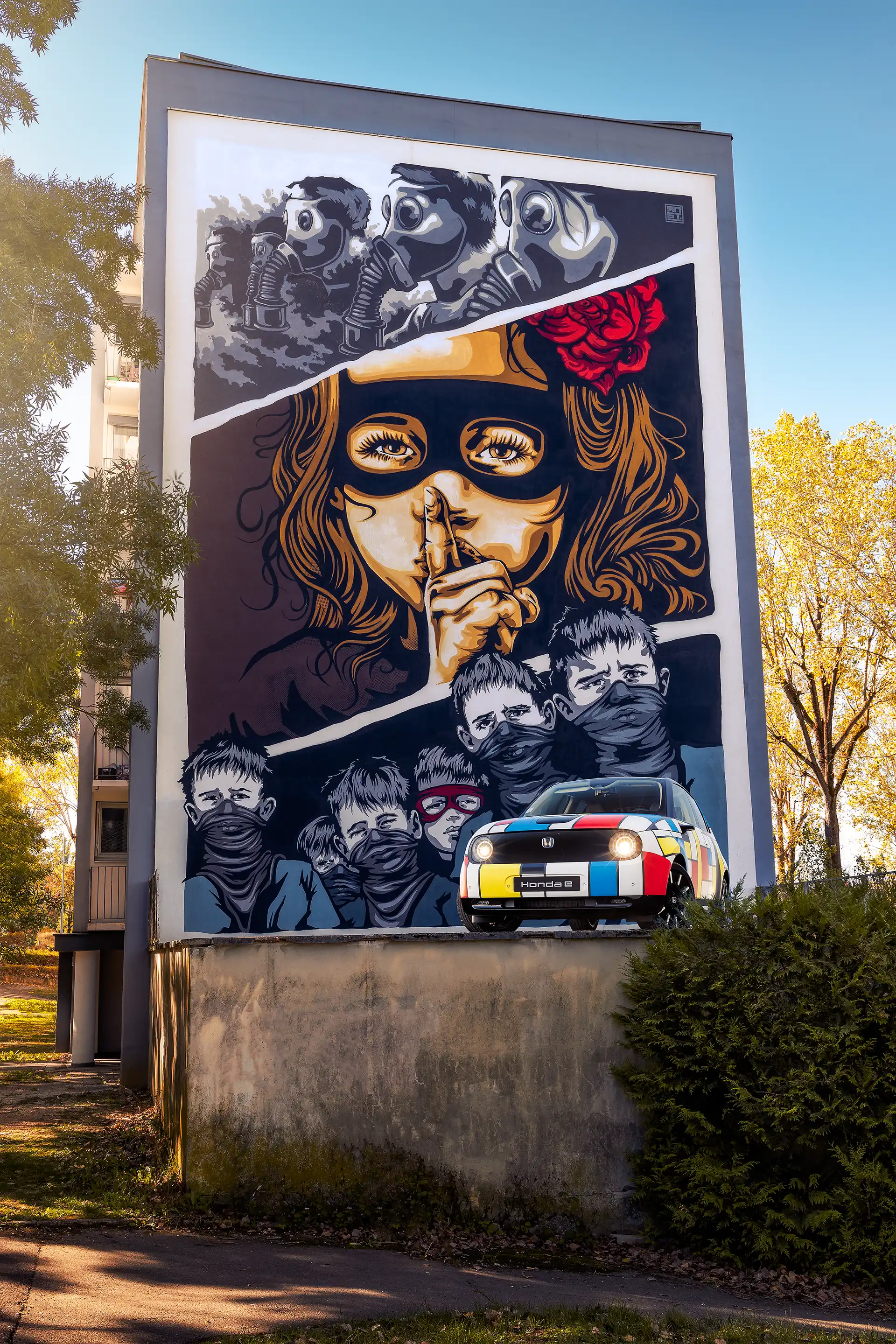 Honda E avec sa déco Mondrian de 3/4 avant devant une œuvre de street art