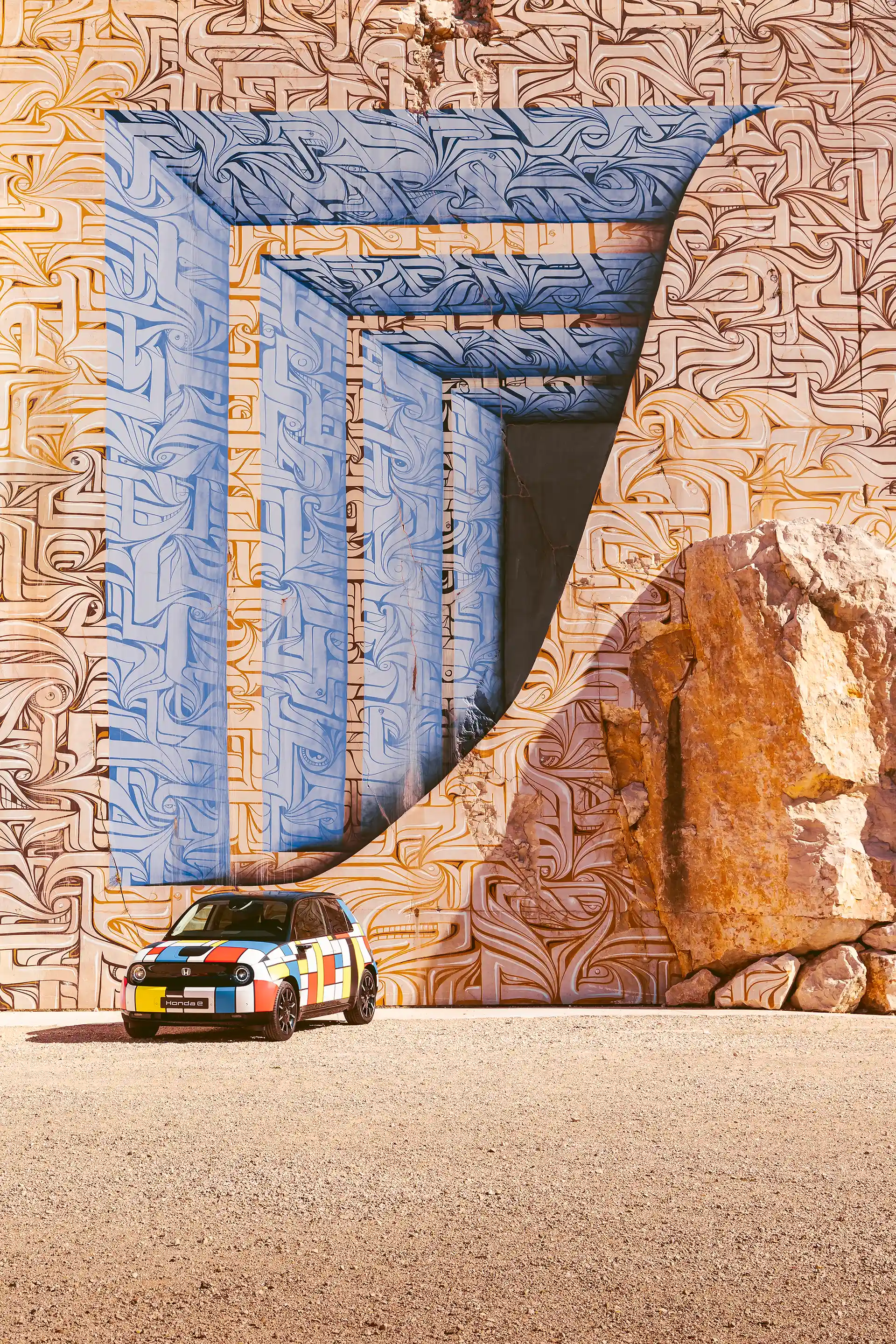 Honda E avec sa déco Mondrian de 3/4 avant devant une œuvre de street art