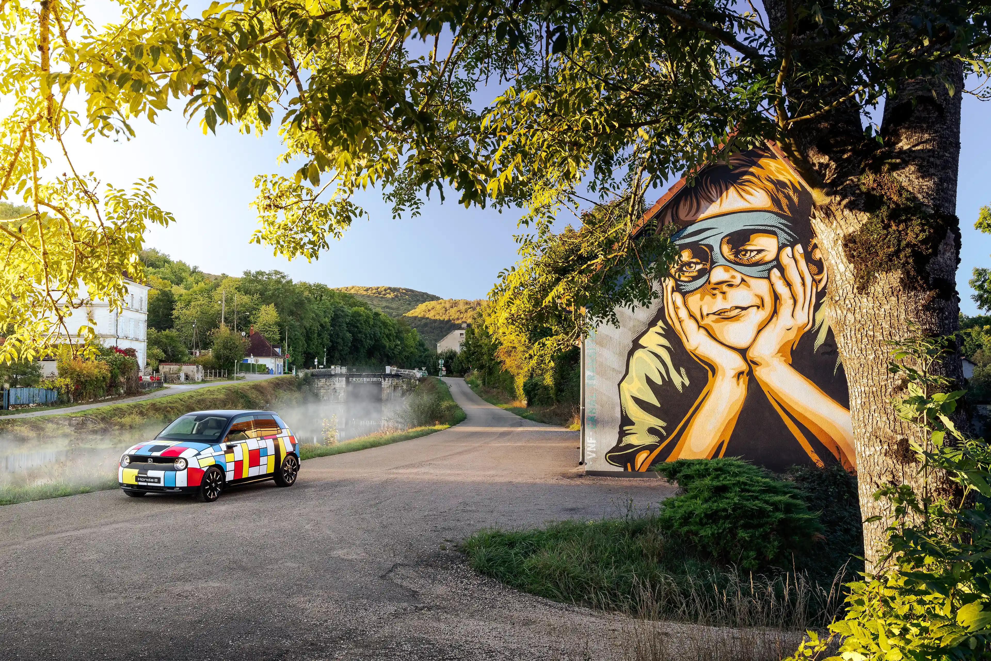 Honda E avec sa déco Mondrian de 3/4 avant devant une œuvre de street art
