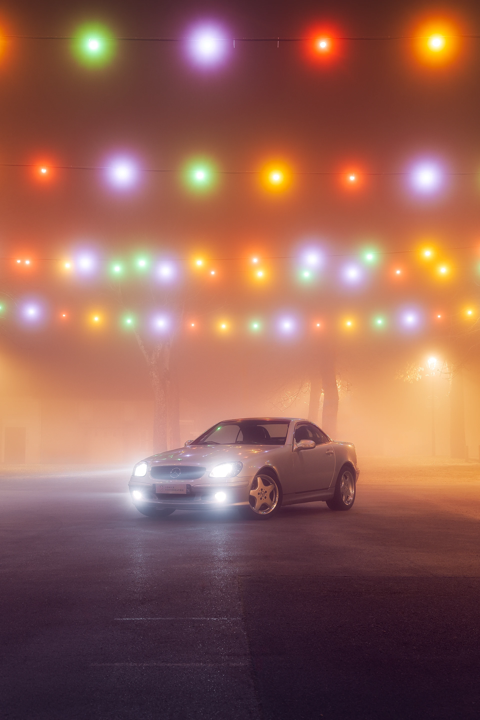 Mercedes SLK R170 grise de 3/4 avant dans le brouillard sous des lampions colorés