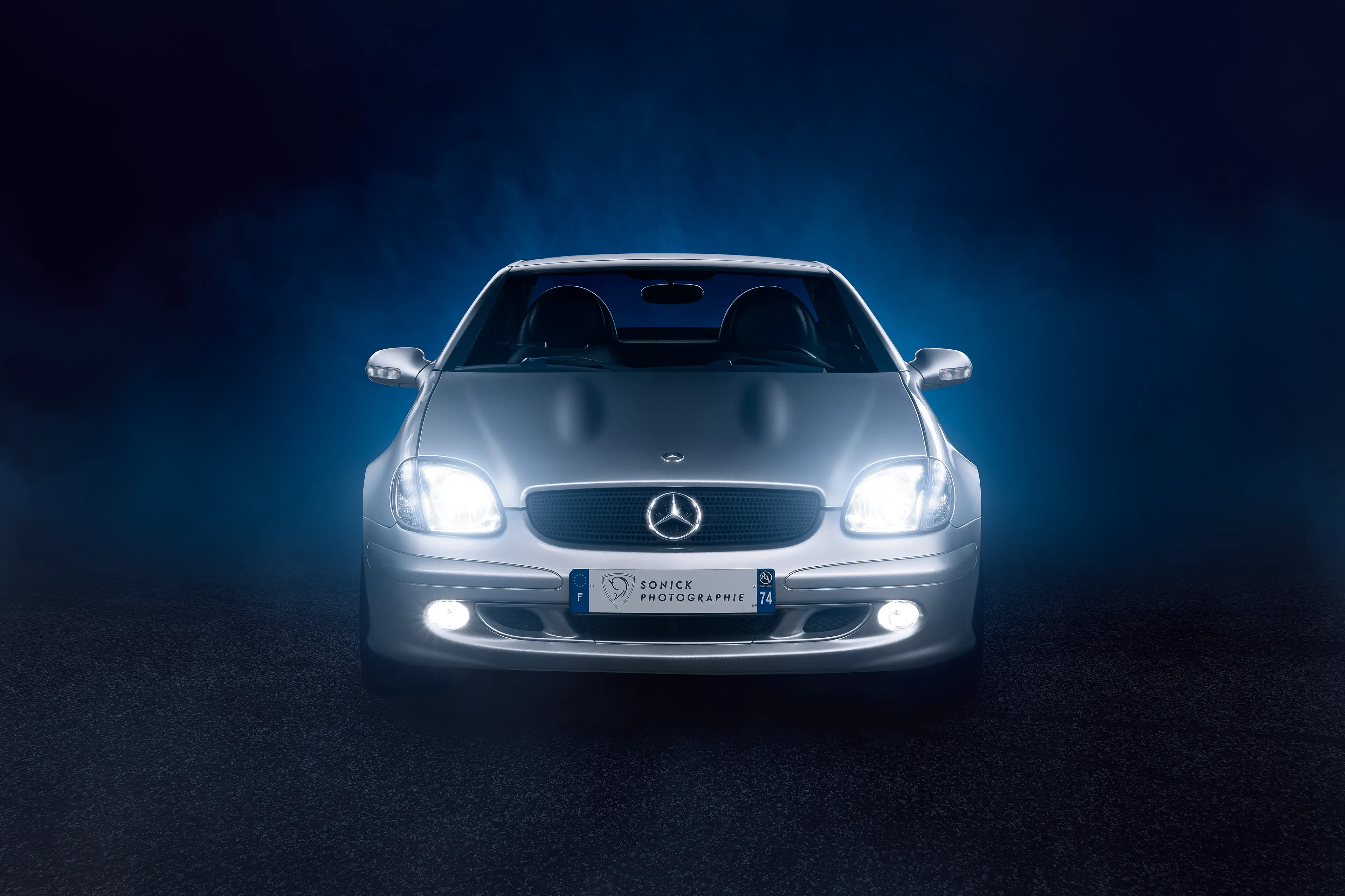 Face avant d'une Mercedes SLK R170 grise dans un brouillard de fumée bleu