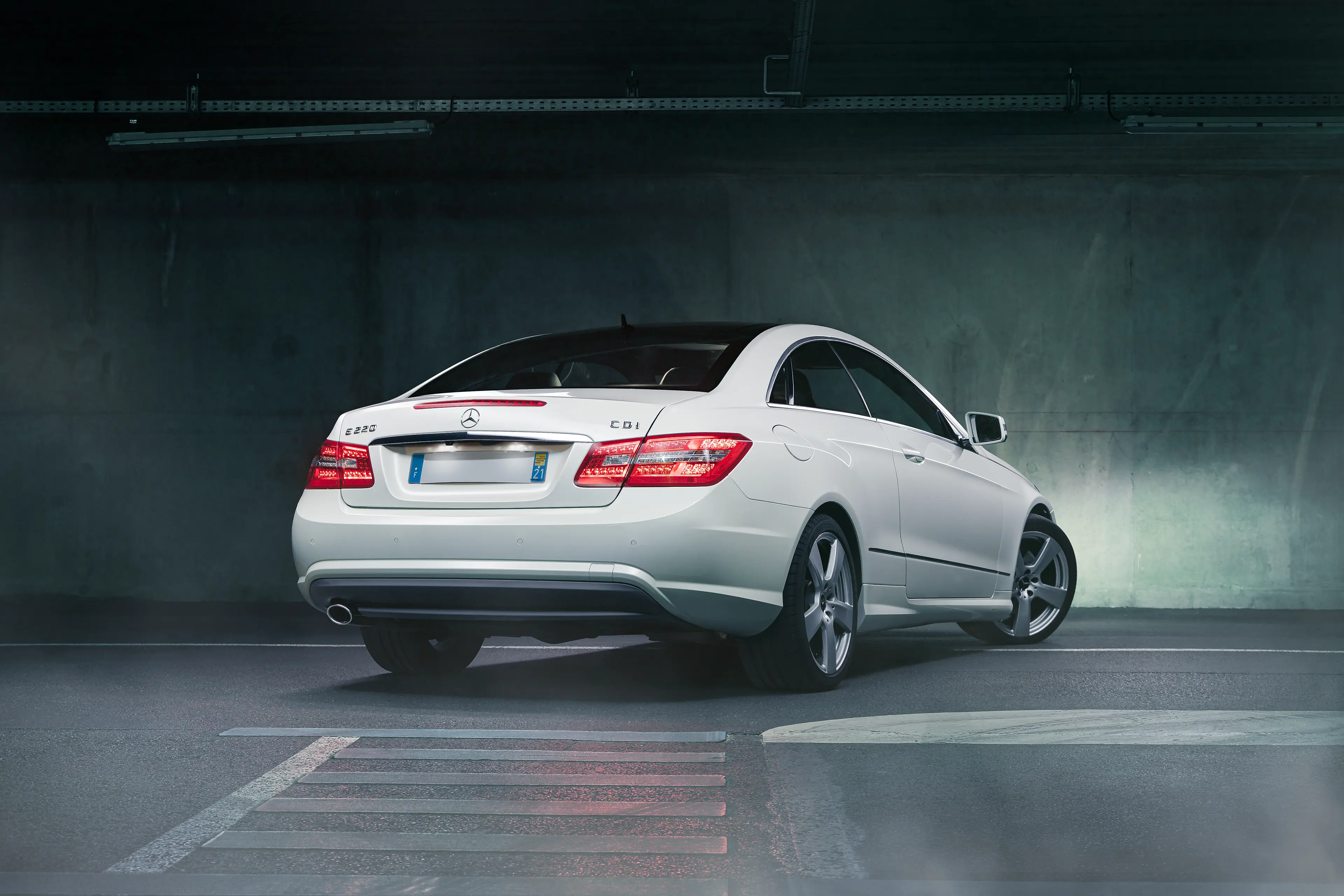 Mercedes Classe E coupé W212 blanche de 3/4 arrière dans un parking sous-terrain en light painting