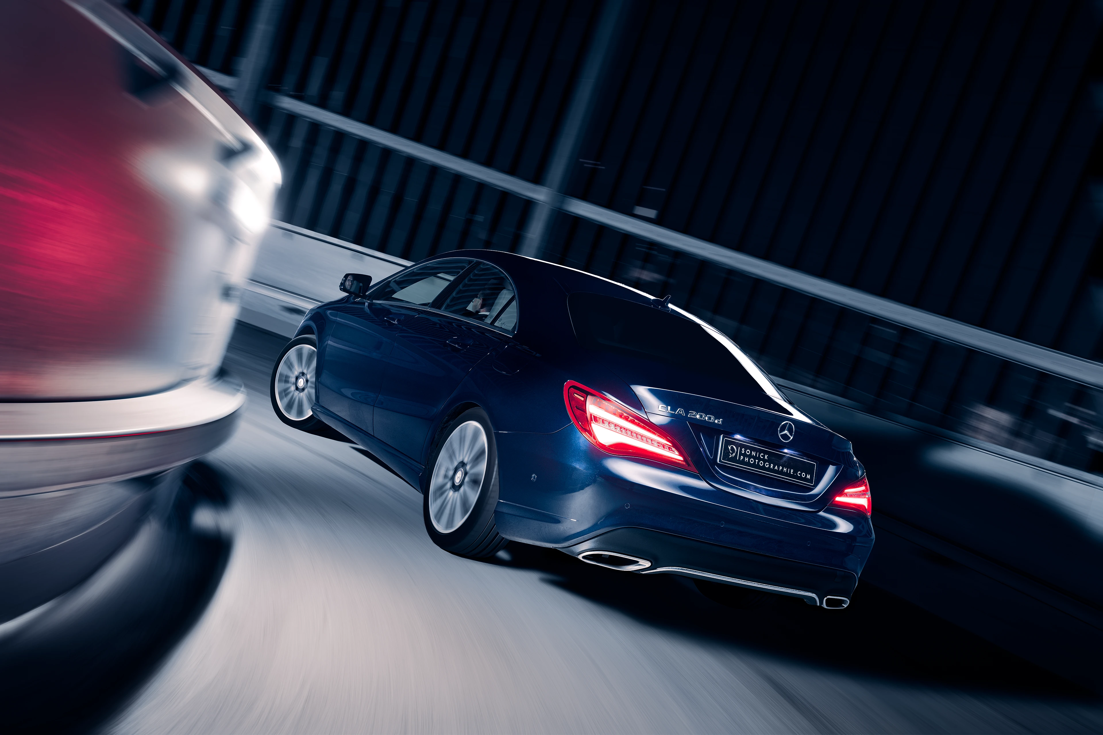 Mercedes CLA bleu foncée de 3/4 arrière en light painting roulant dans un parking de nuit dans un collimaçon