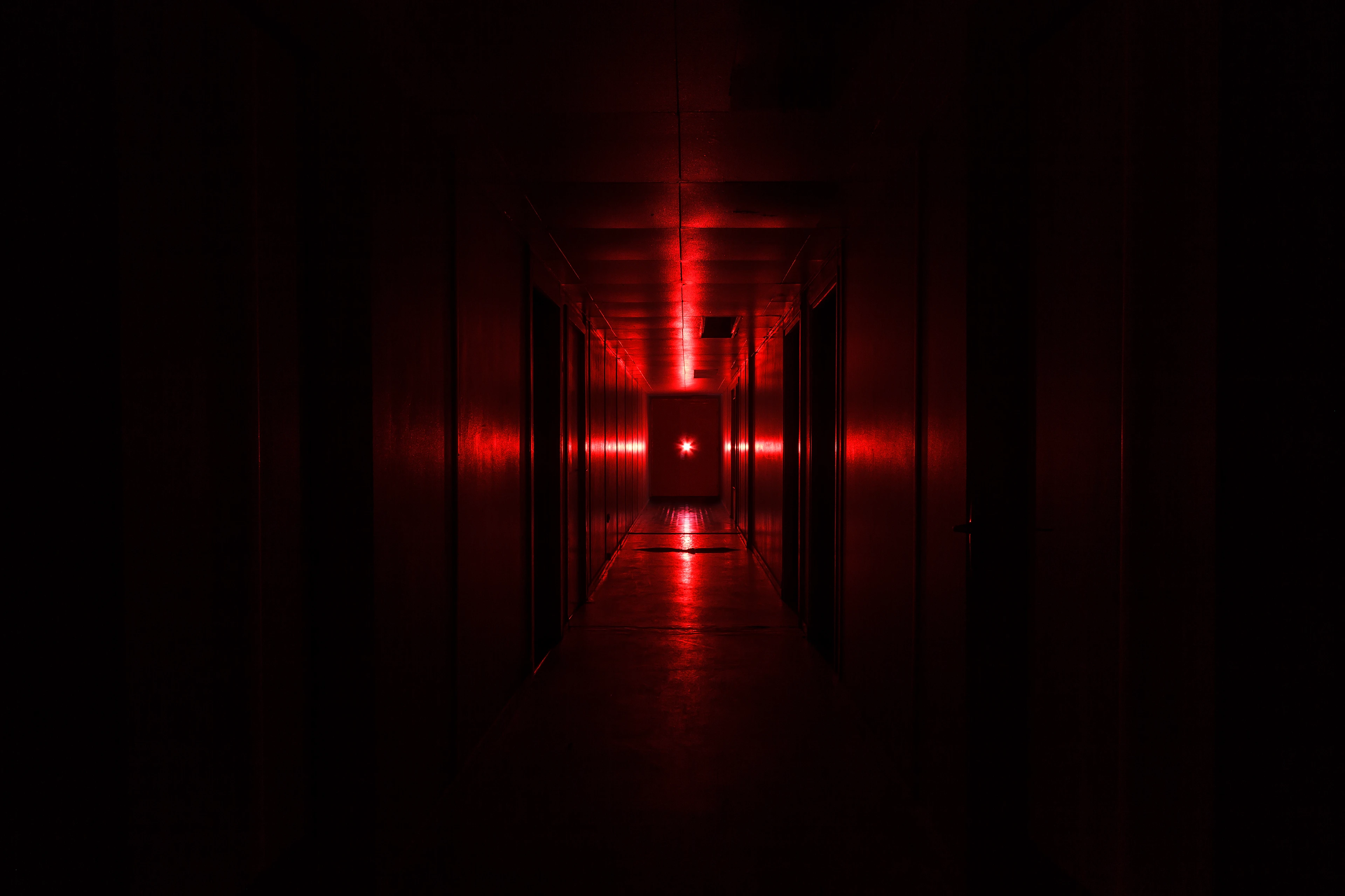 Photo sombre d'un couloir éclairé par une lumière rouge qui reflète en forme de croix sur les murs