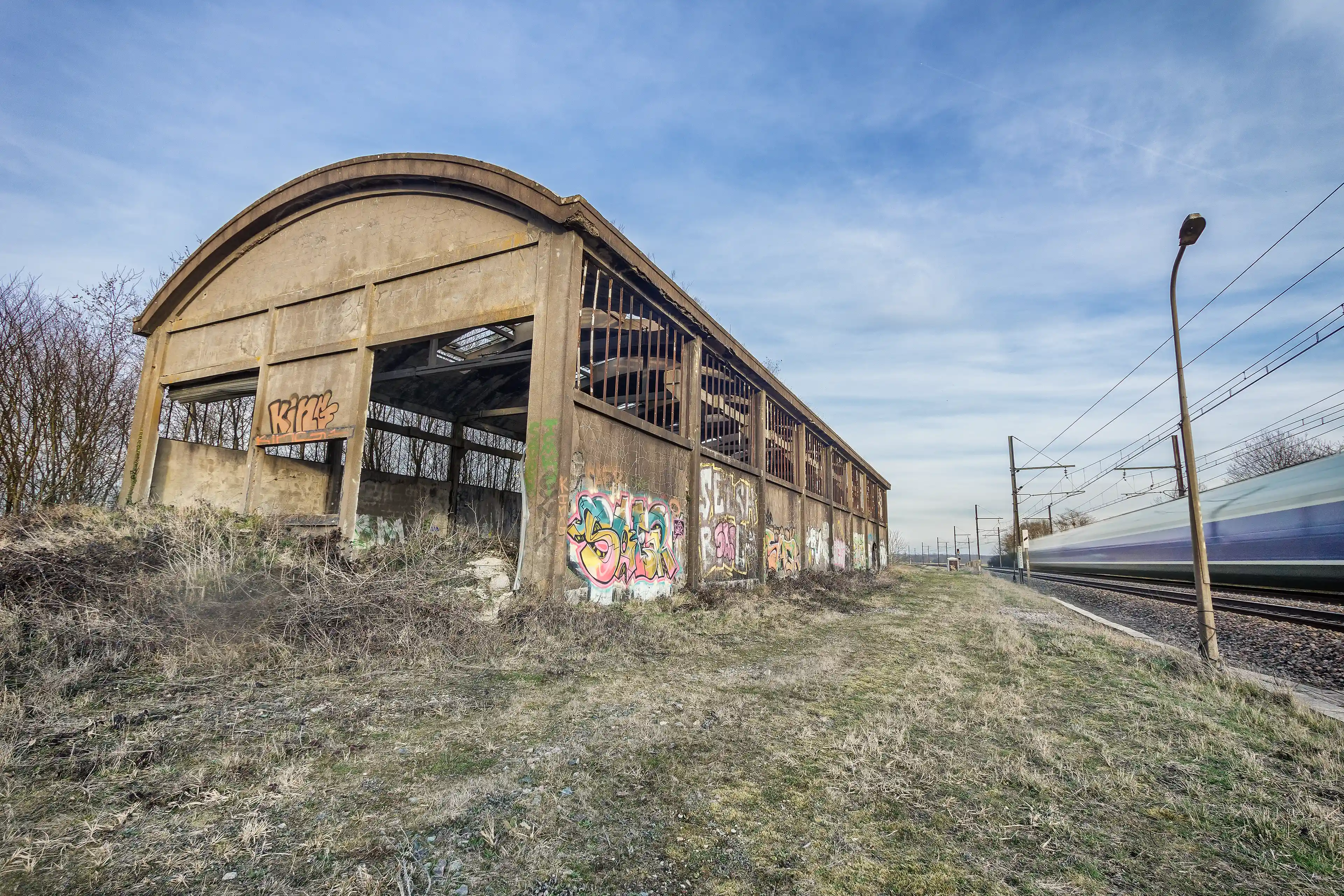 Photo urbex d'un entrepôt délabré avec des tags et un train qui passe en pose longue