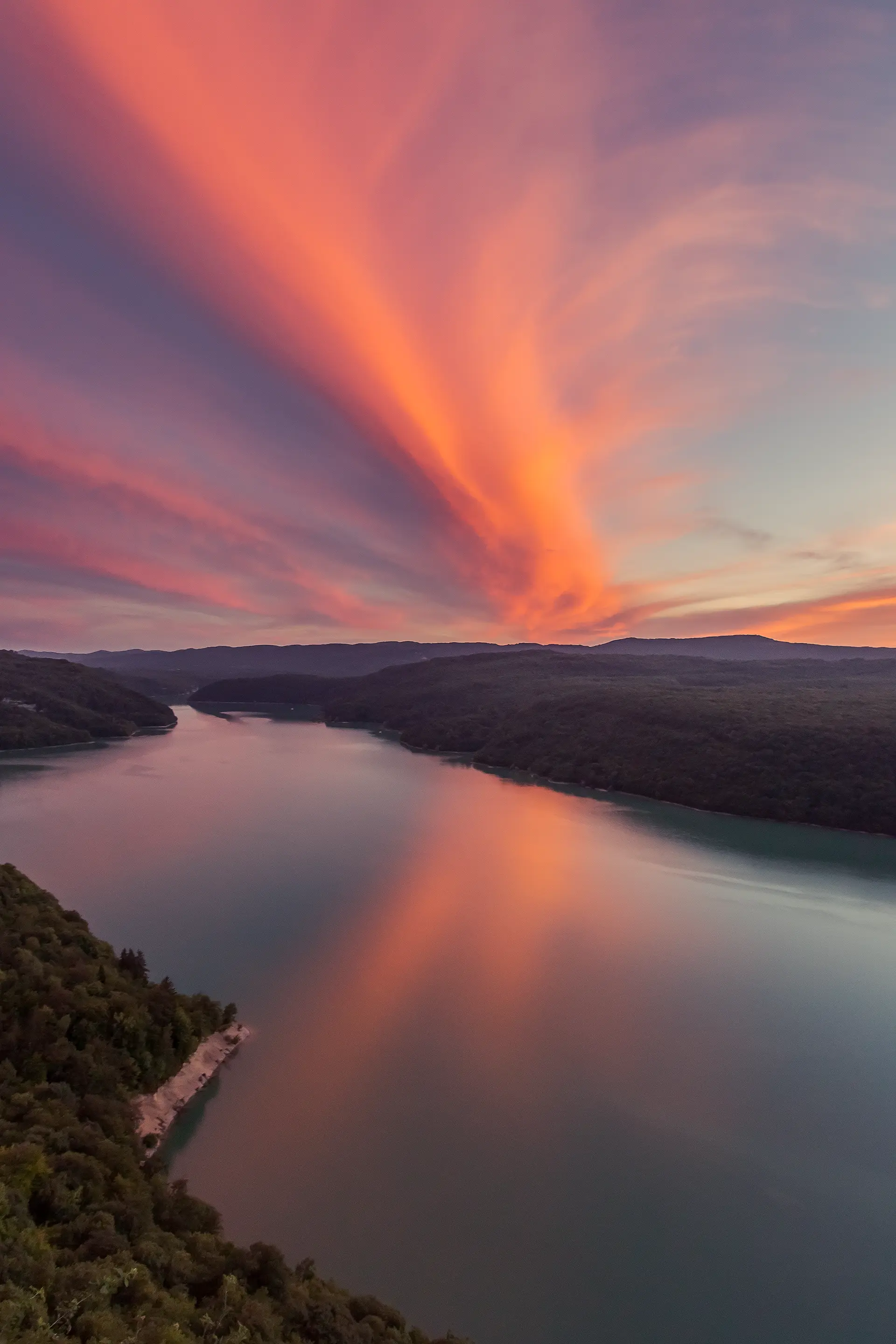 Lac de Vouglans dans le Jura avec un grand nuage orangé dans le ciel qui se reflète dans l'eau