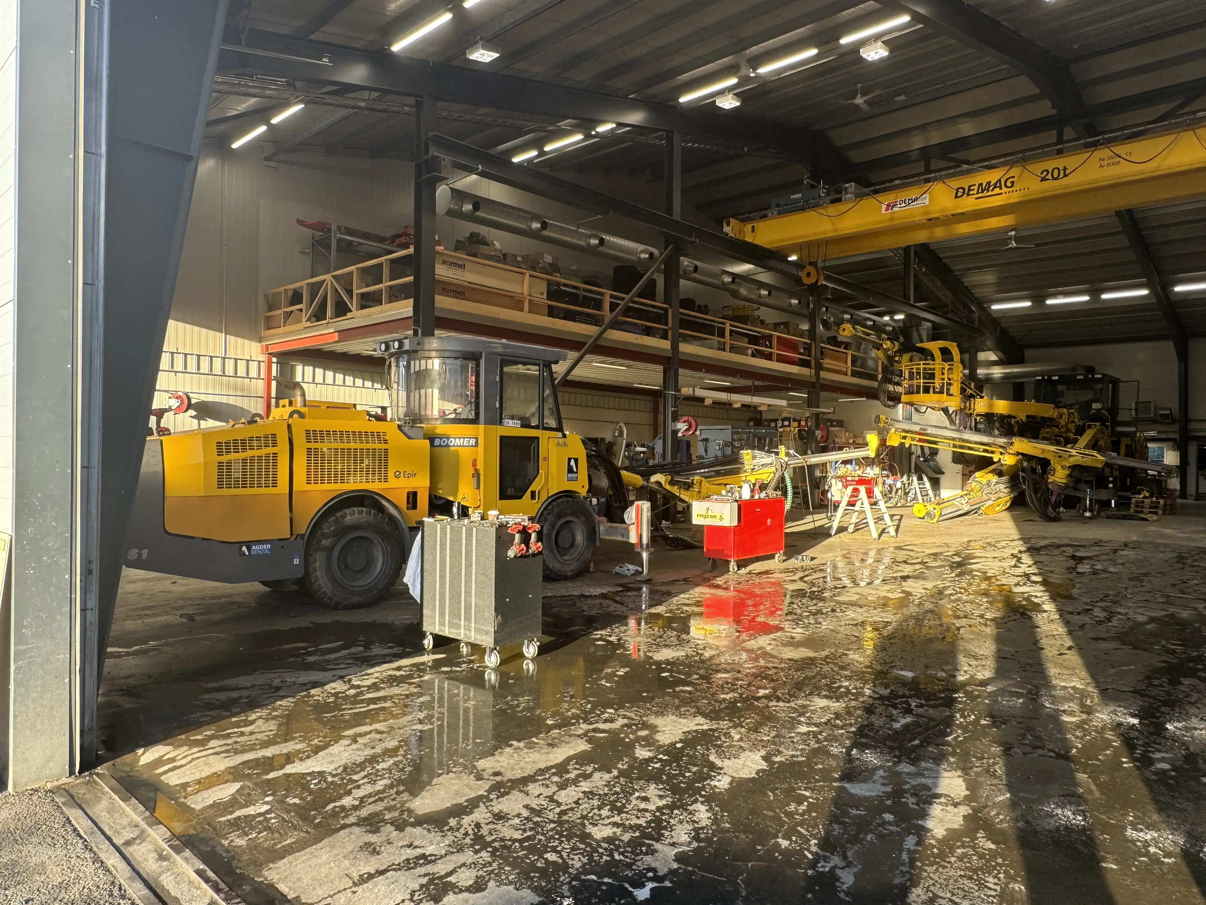 Gul byggeutstyr og maskiner plassert inne i en lys, industribygg med betonggulv.