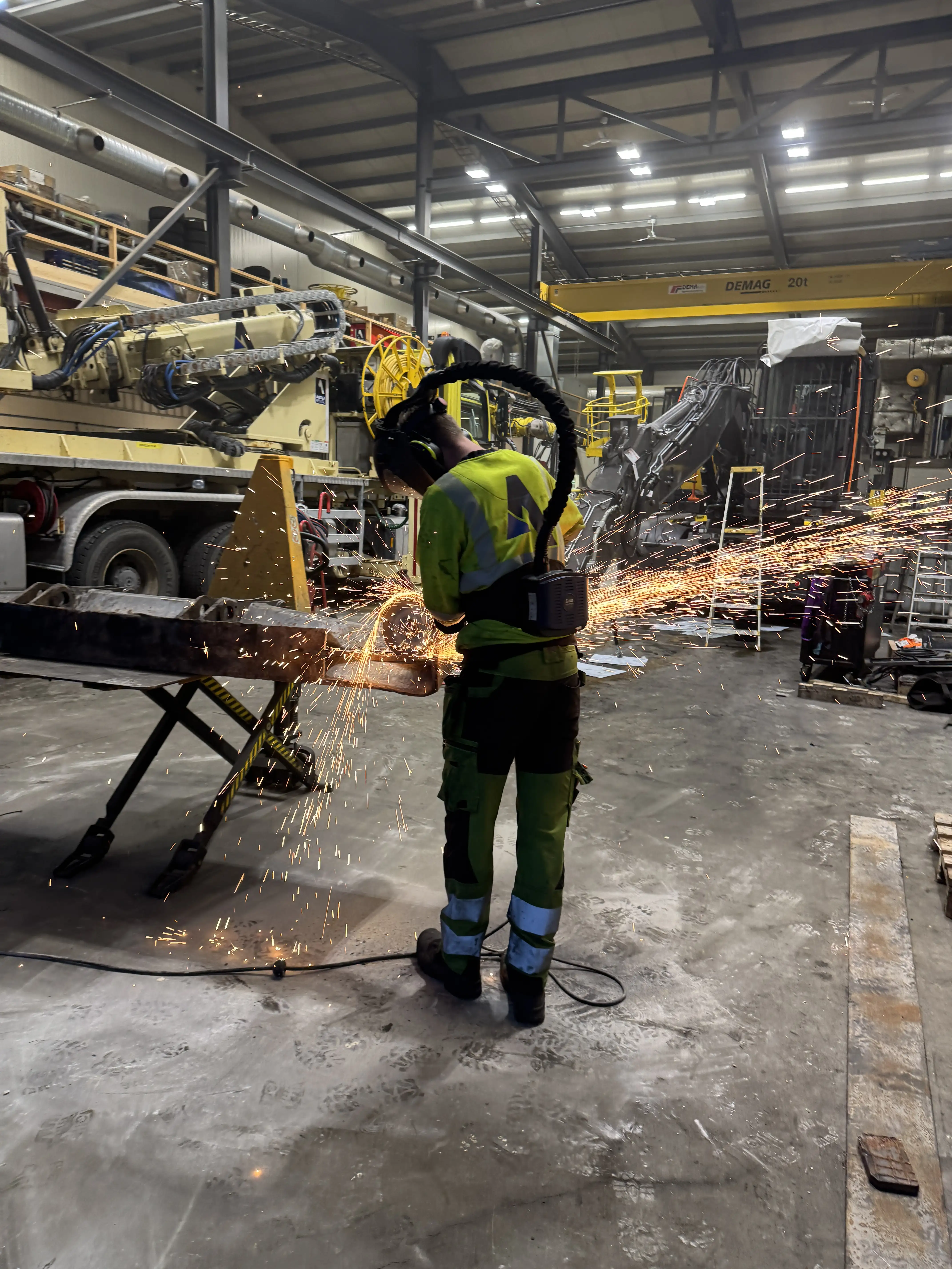 Arbeider i verneskjerm og verneutstyr som bruker slipemaskin i en industribygning, med gnister som flyr.