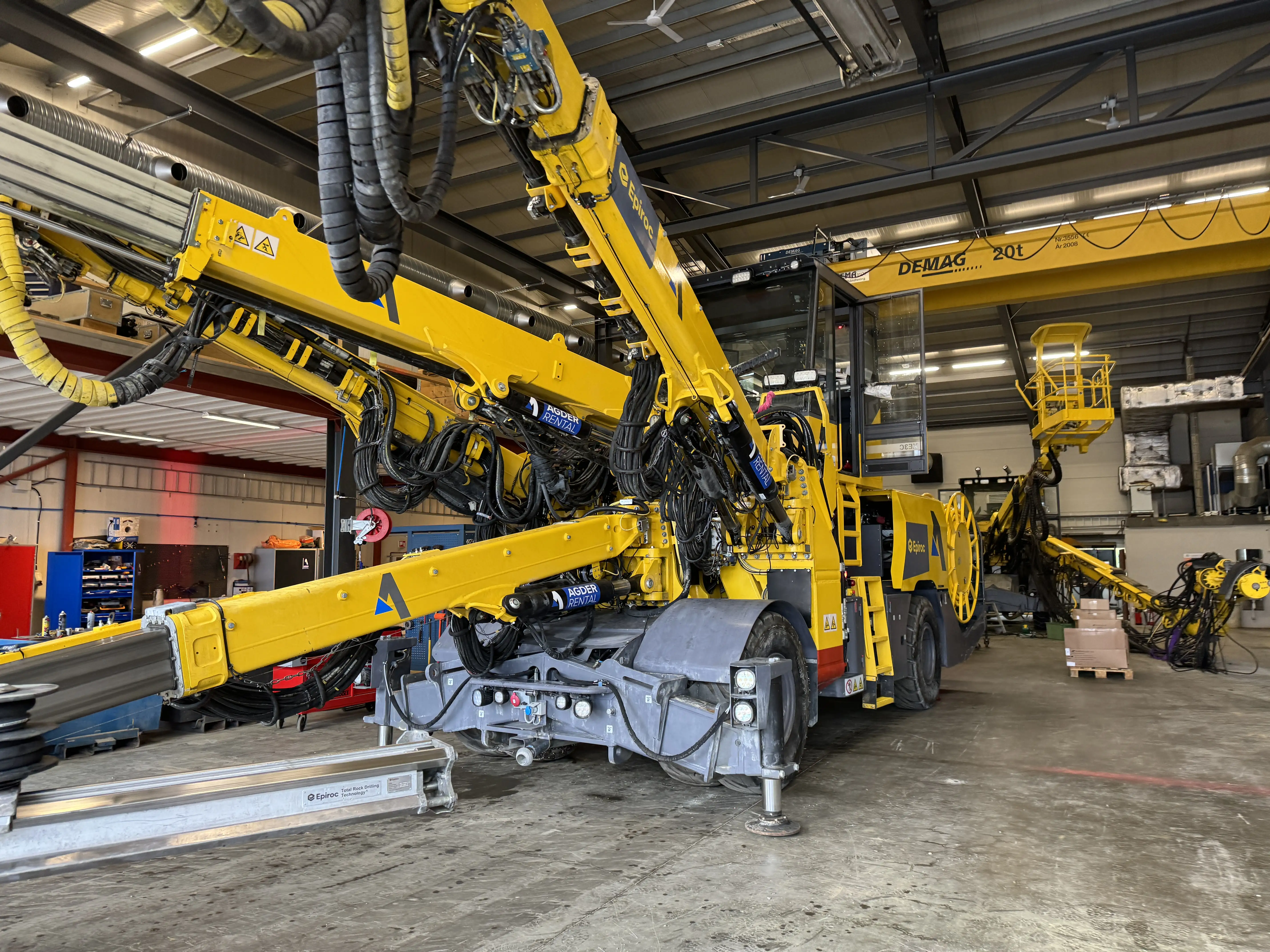 Stor gul boremaskin med flere hydrauliske armer plassert i en industribygg.
