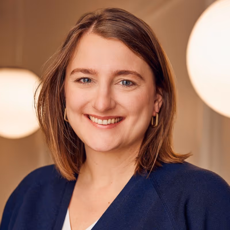 Professional headshot of Tori Hellrung, smiling woman with shoulder-length light brown hair, wearing a dark blue sweater, with warm lighting in the background.