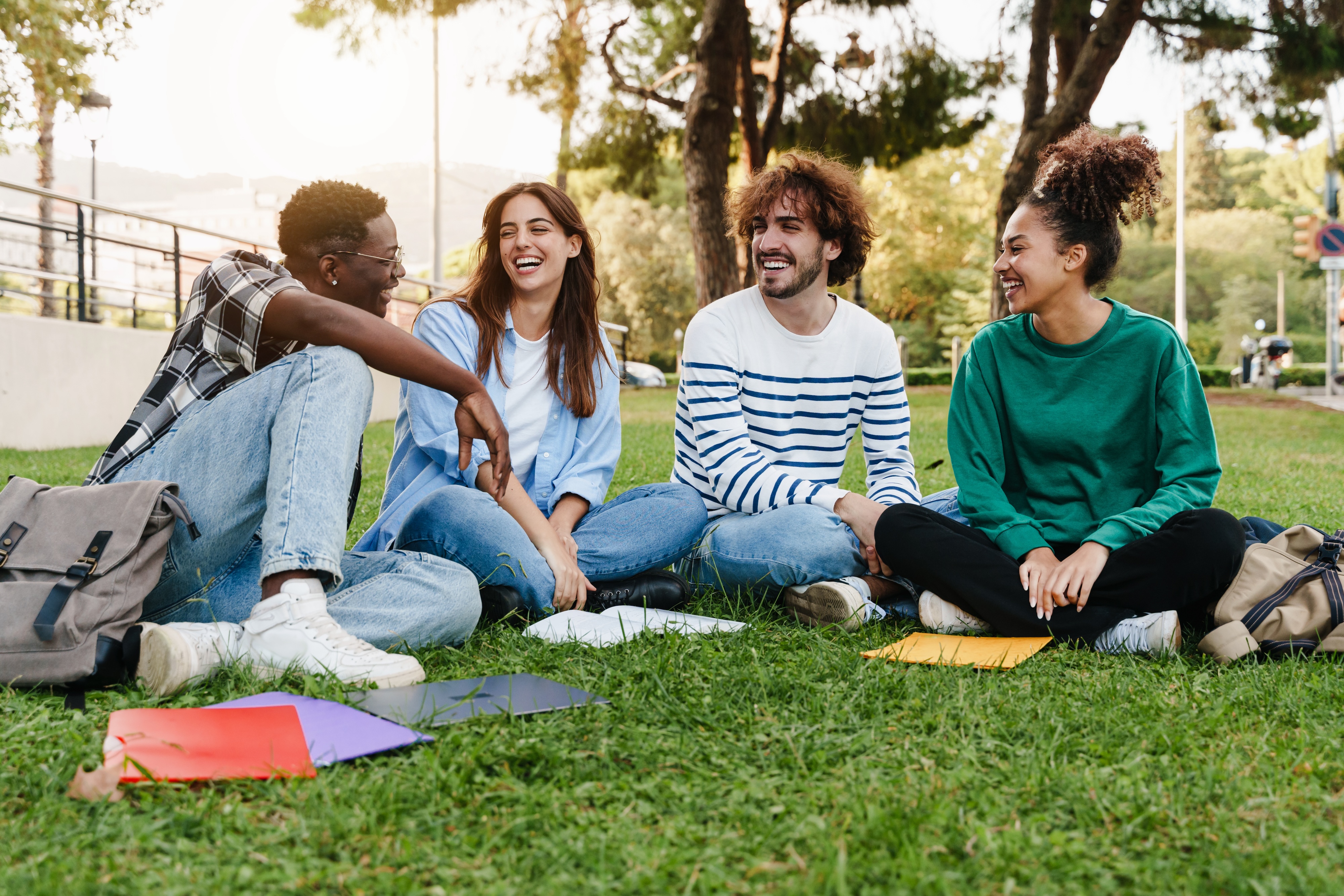 Group of happy students laughing and socializing on the grass outdoors, representing the vibrant community at Global College Station in College Station, TX.