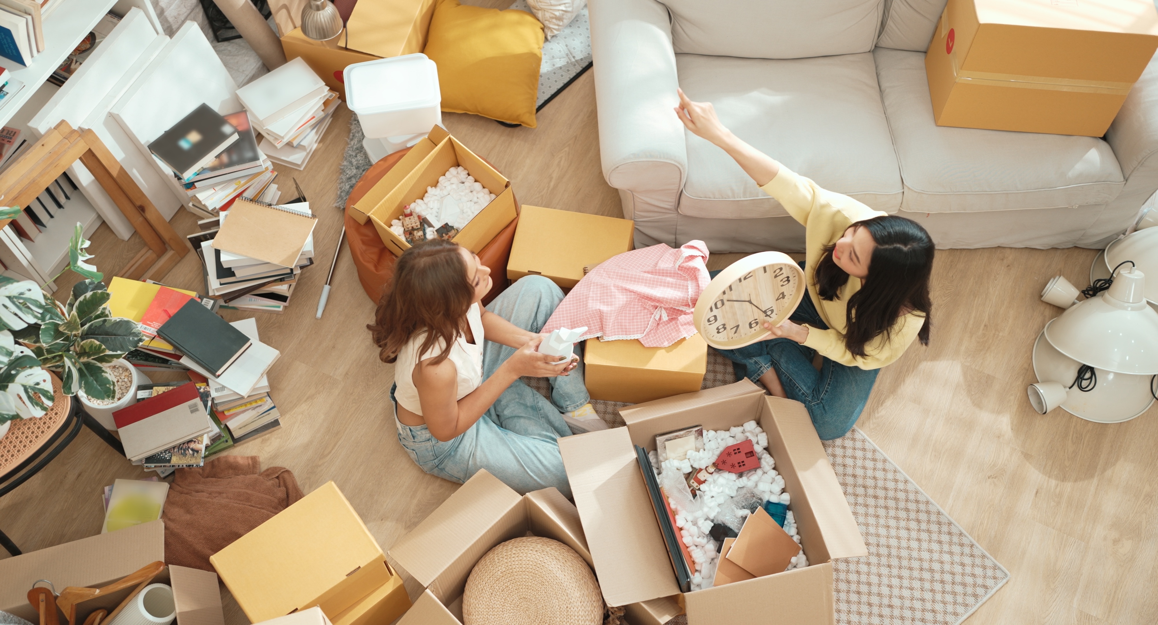 Two happy young women unpacking moving boxes and decorating their new apartment, depicting the excitement of moving into Global College Station in College Station, TX.