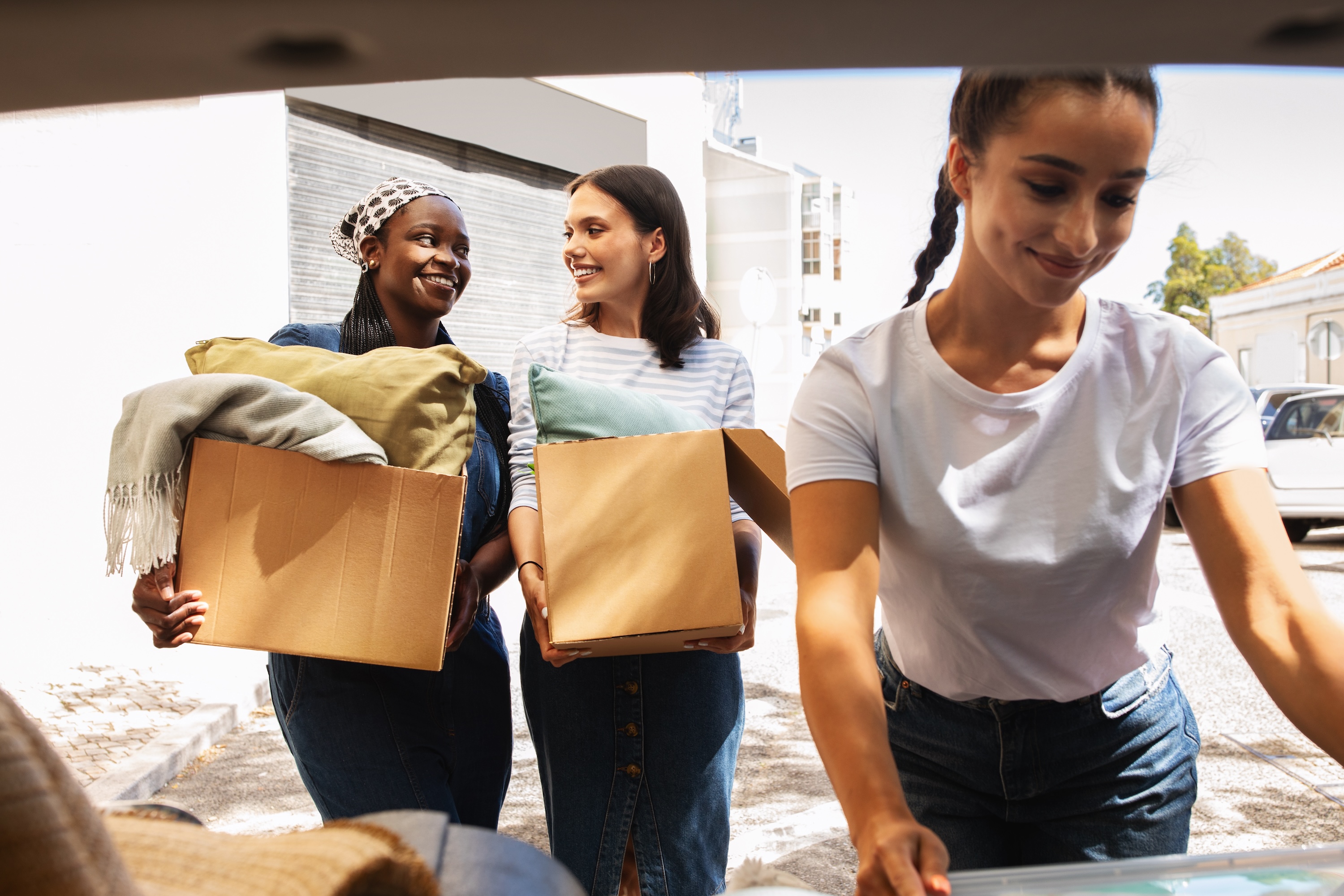 A group of female students happily moving boxes and pillows out of a car, representing the community and easy move-in process at Global College Station in College Station, TX.
