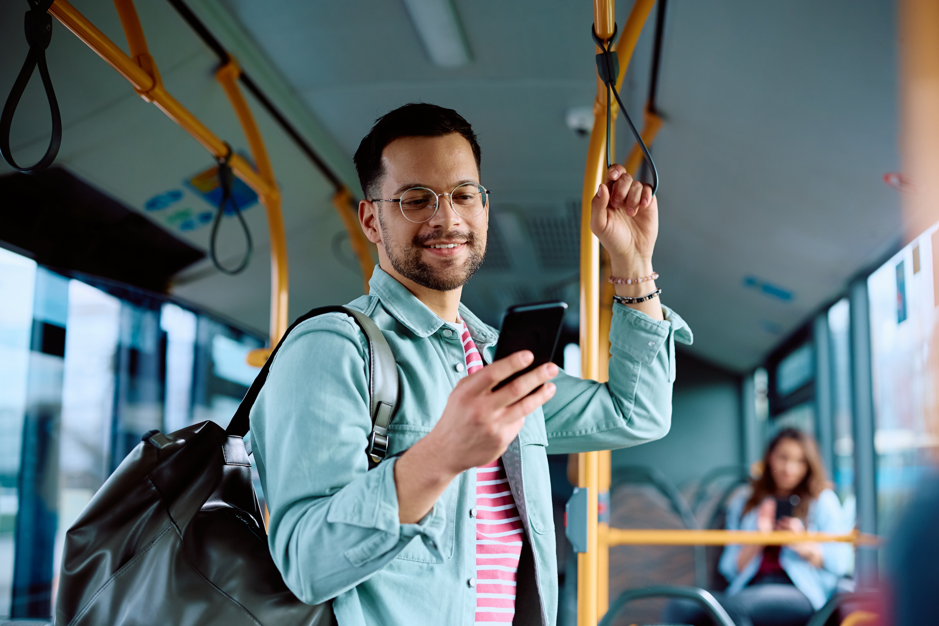 A resident with a backpack smiling while using a smartphone on public transit near Global College Station, showcasing easy commuting and urban connectivity in College Station, TX.
