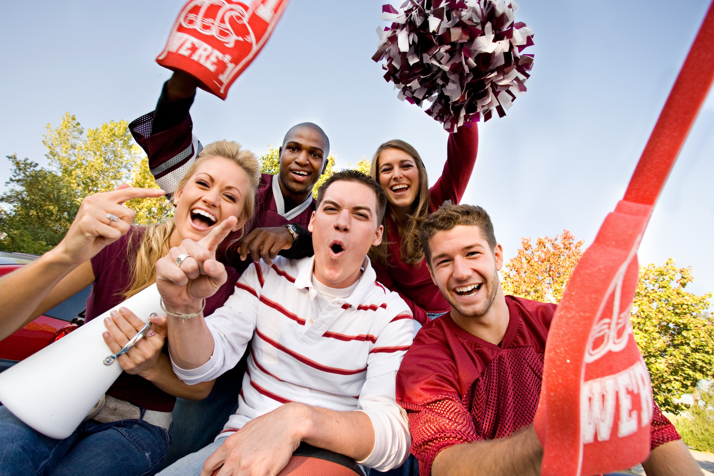 Fans cheering with pom-poms and a foam finger at a tailgate near Global College Station