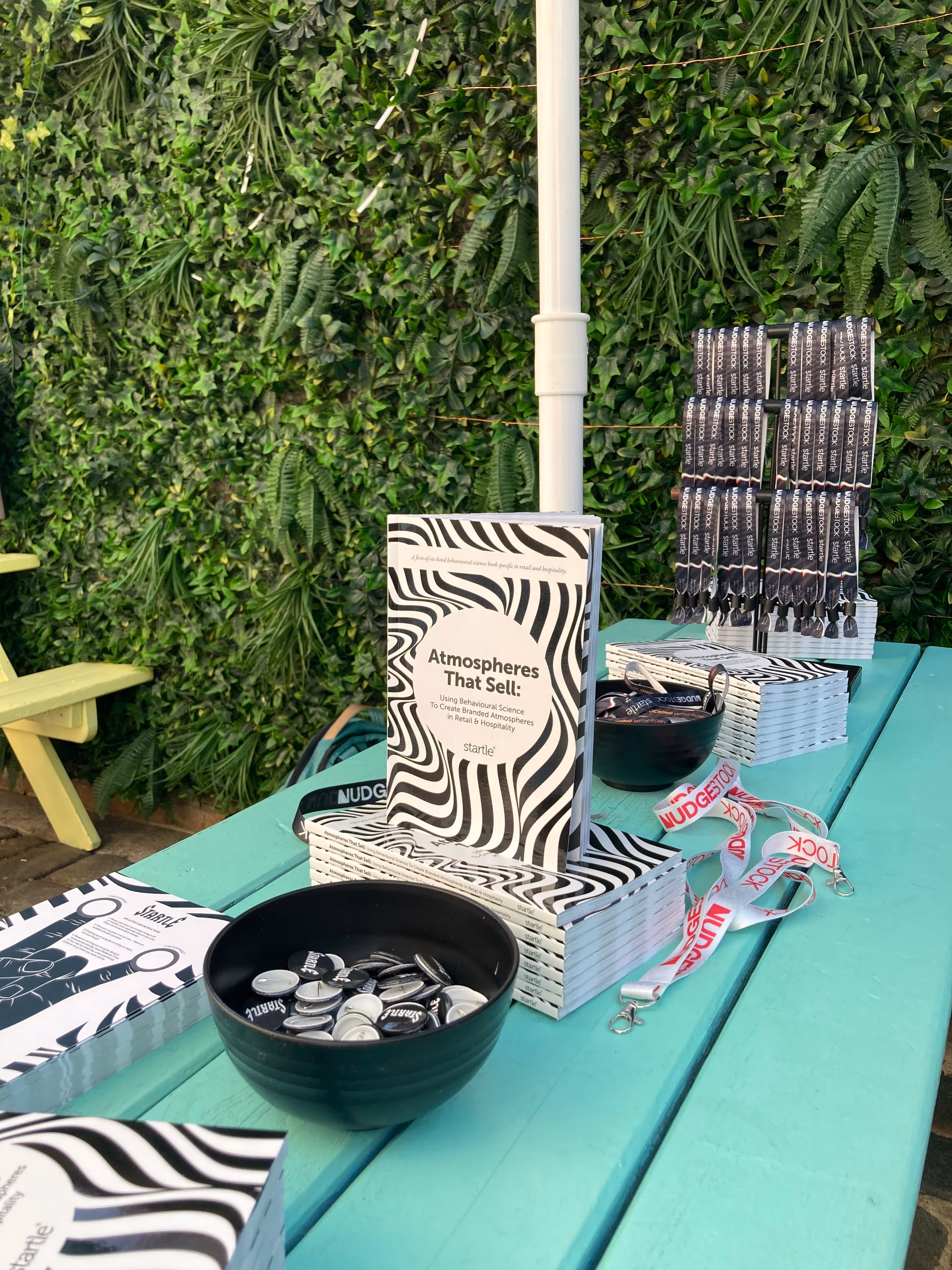 Atmospheres That Sell books, Startle wristbands, lanyards and badges on a green picnic table