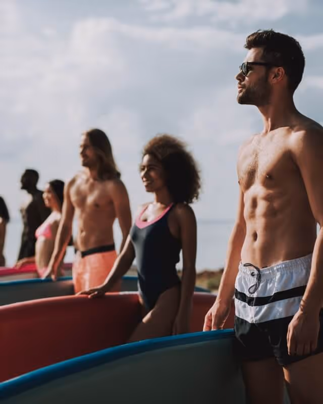 A group of people in swimwear on the beach holding surf boards