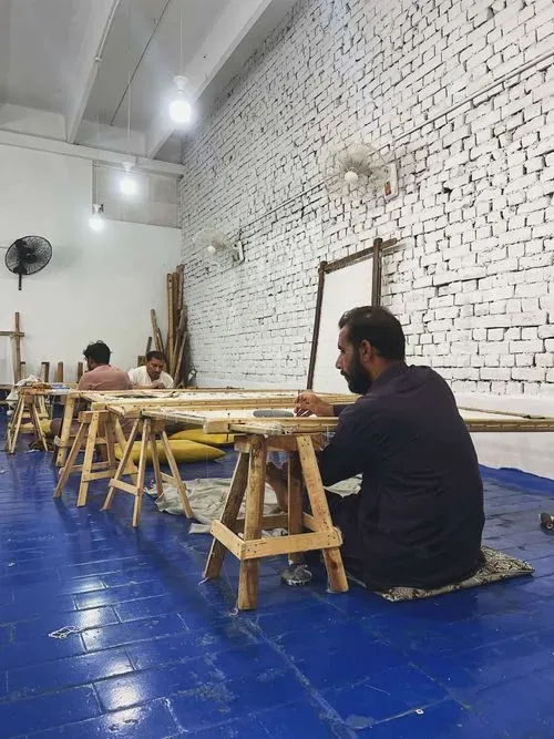 An image from behind of a person threading a stretched fabric while another person works in the distance