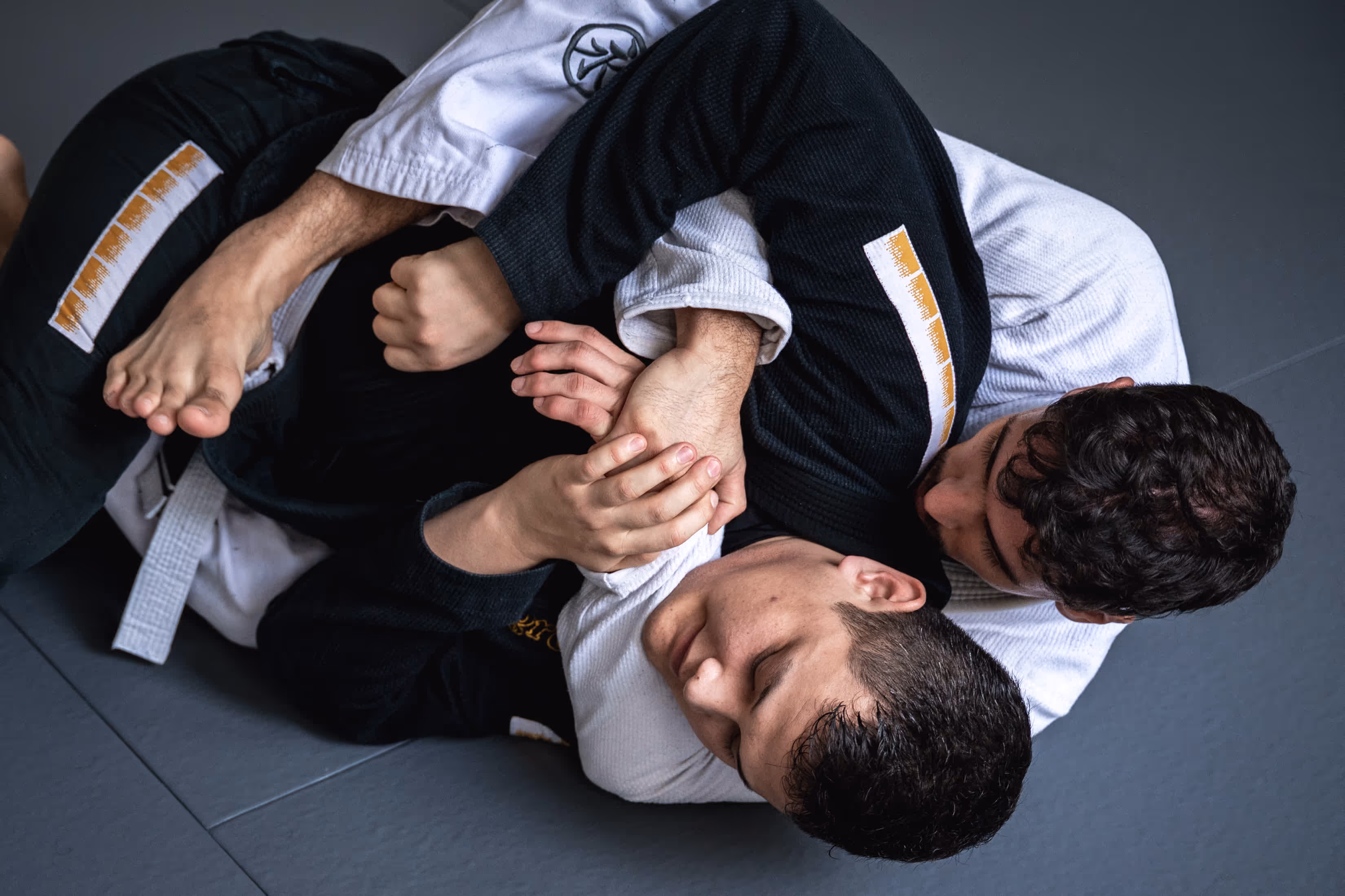 BJJ-Schüler in schwarzen und weißen Gis trainieren Hebel- und Kontrolltechniken unter Anleitung eines Trainers.