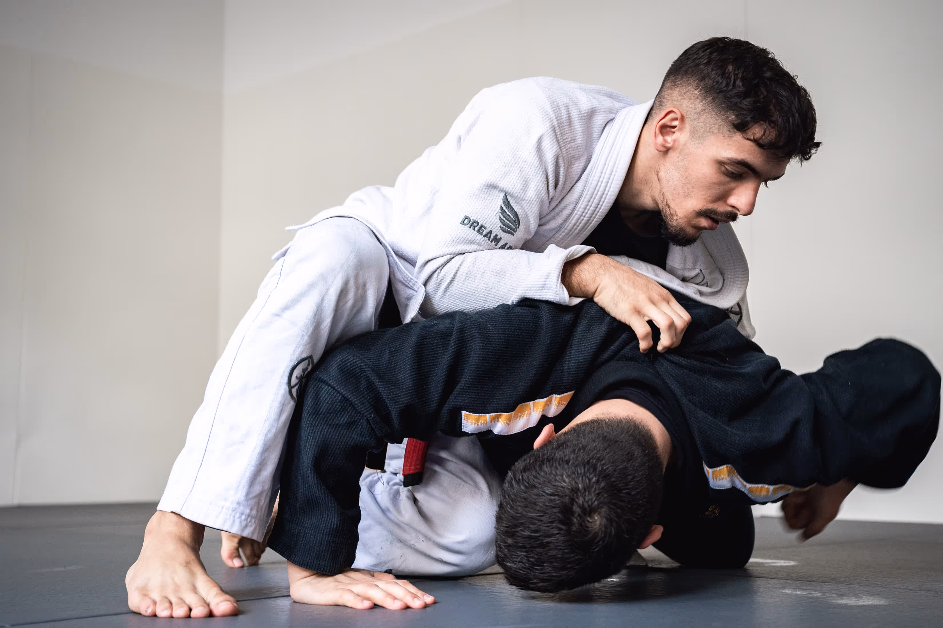 Zwei BJJ-Kämpfer in weißem und schwarzem Gi üben eine Kontrolltechnik während eines Trainings im Dream Art Dojo.