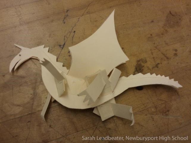 White paper sculpture of a dragon or creature on textured brown surface