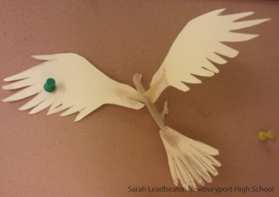 Cream-colored paper dove with green eye and spread wings flying against brown background