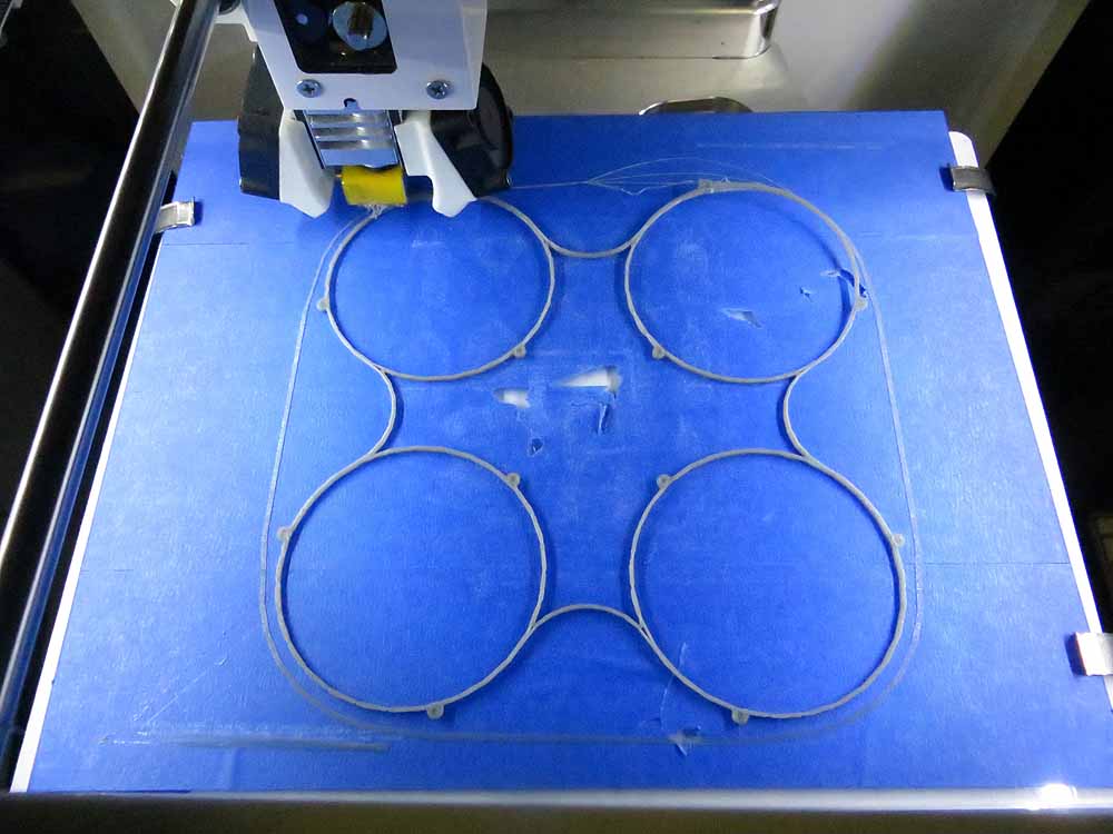 3D printer printing circular patterns on blue platform with printing head visible above