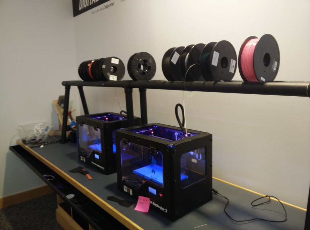 3D printers with spools of filament on shelf above them in workshop