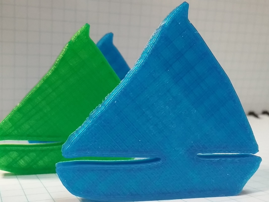 Two colorful plastic toy sailboats, one green and one blue, positioned together.