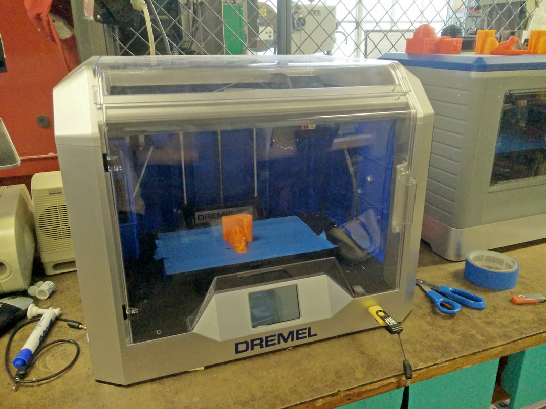 Dremel 3D printer with blue interior and orange object printing on workbench