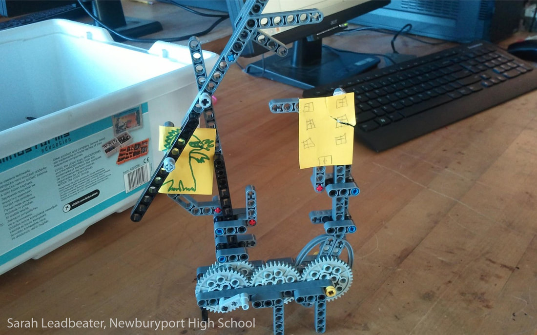 Robotic arm made of metal construction pieces with yellow sticky notes attached on desktop.