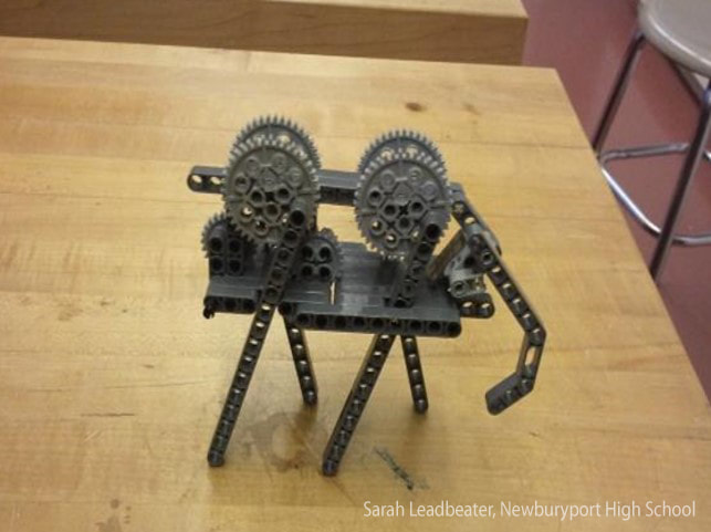 Mechanical robot made from gears and metal parts resembling an insect on wooden surface.