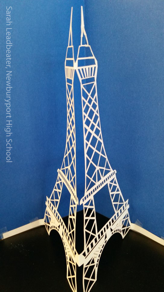 White paper cut model of tall twin-spire cathedral tower against blue background