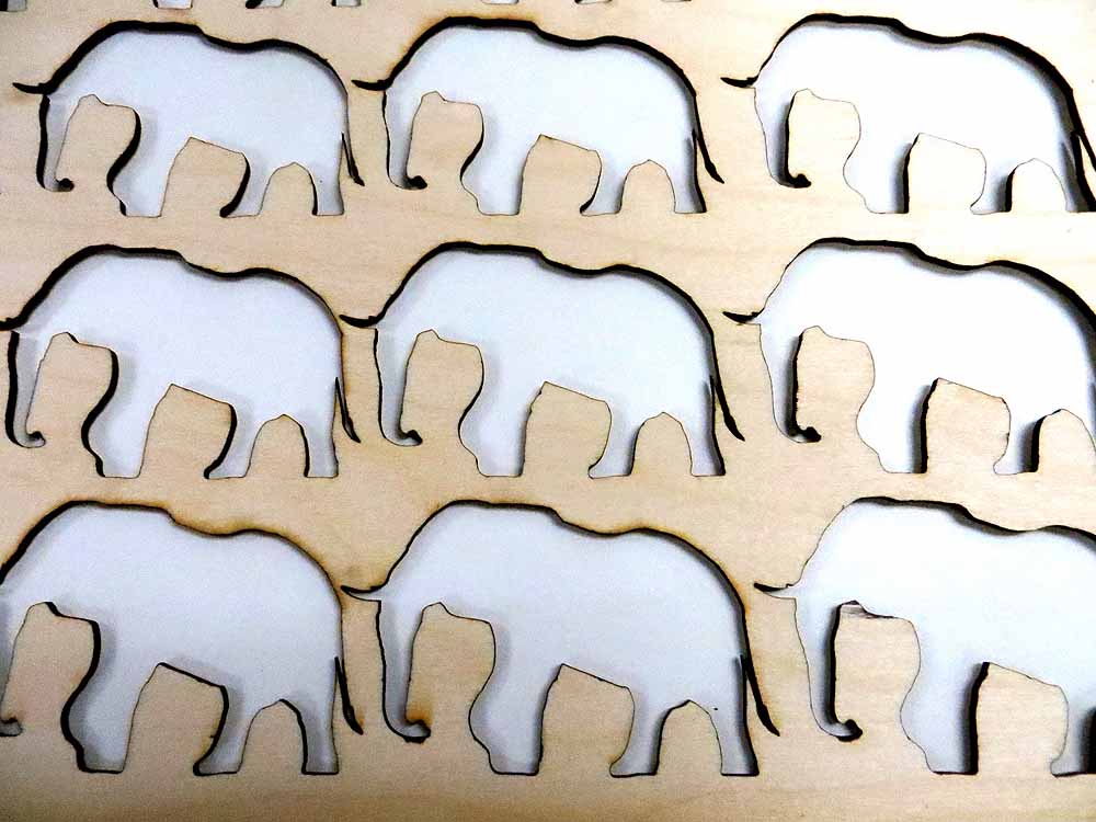 Laser-cut wooden elephant family puzzle pieces arranged in grid pattern with shadows.