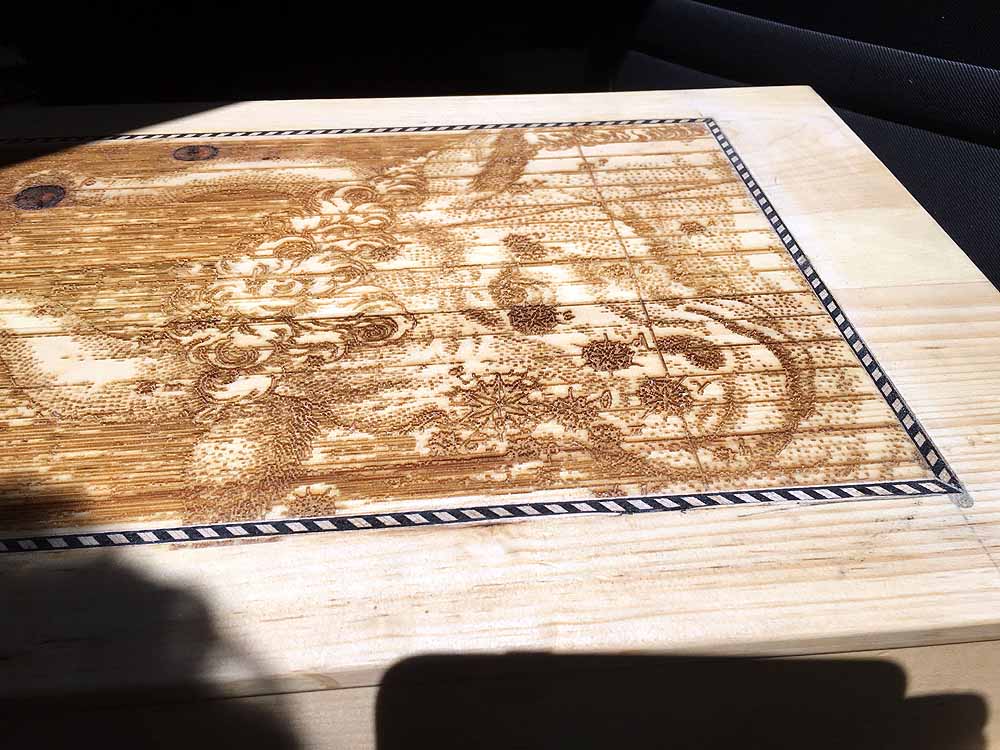 Wood-burned nautical map with intricate sea creatures and compass design on wooden board