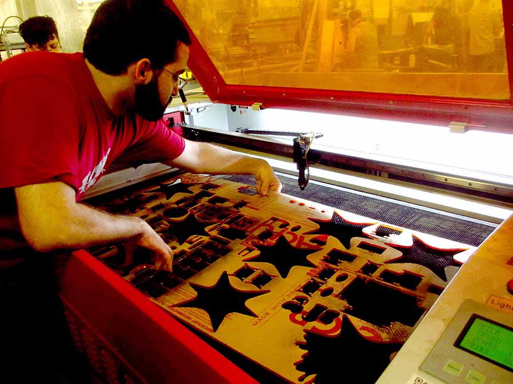 Man operating laser engraving machine cutting yellow material with text design