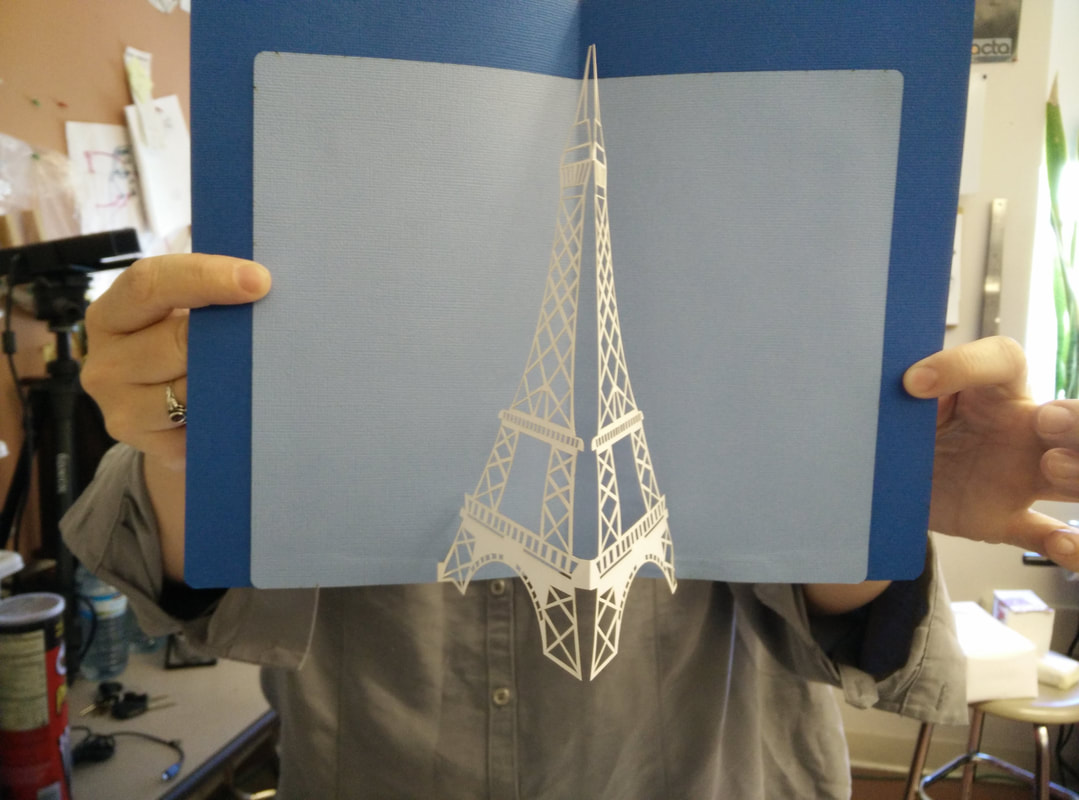 Person holding blue notebook with white Eiffel Tower illustration in office setting